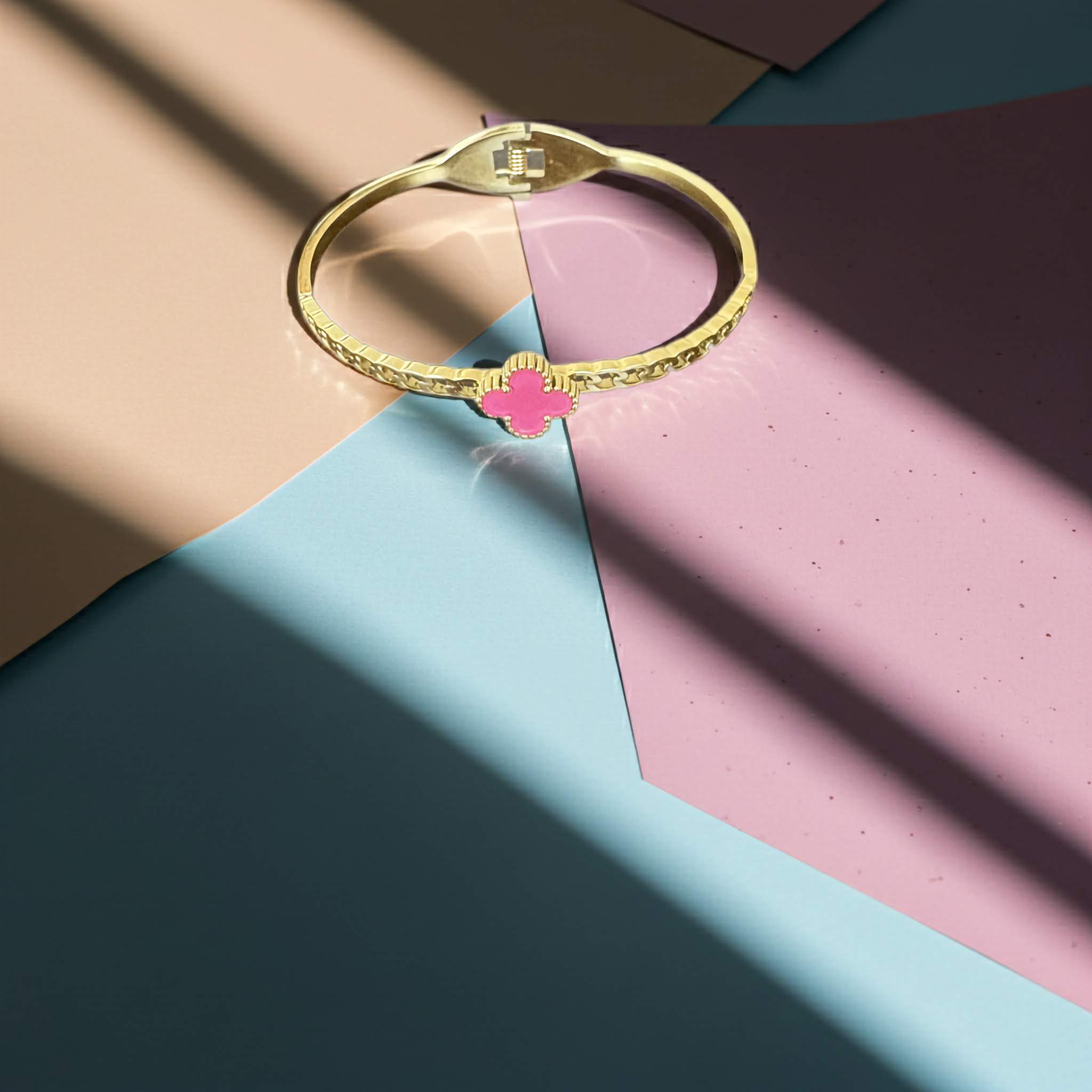 18k Gold plated bracelet with a pink clover charm on a tri-colour paper background