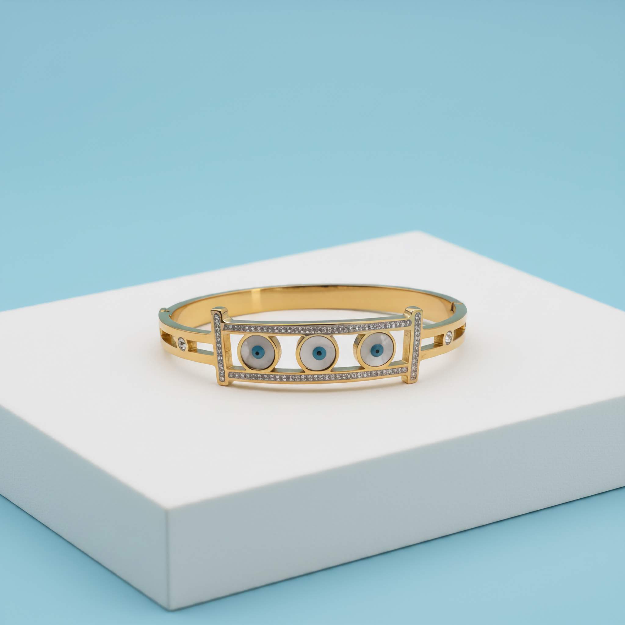 18k Gold plated bracelet with blue evil eye stones on a white platform against a light blue background