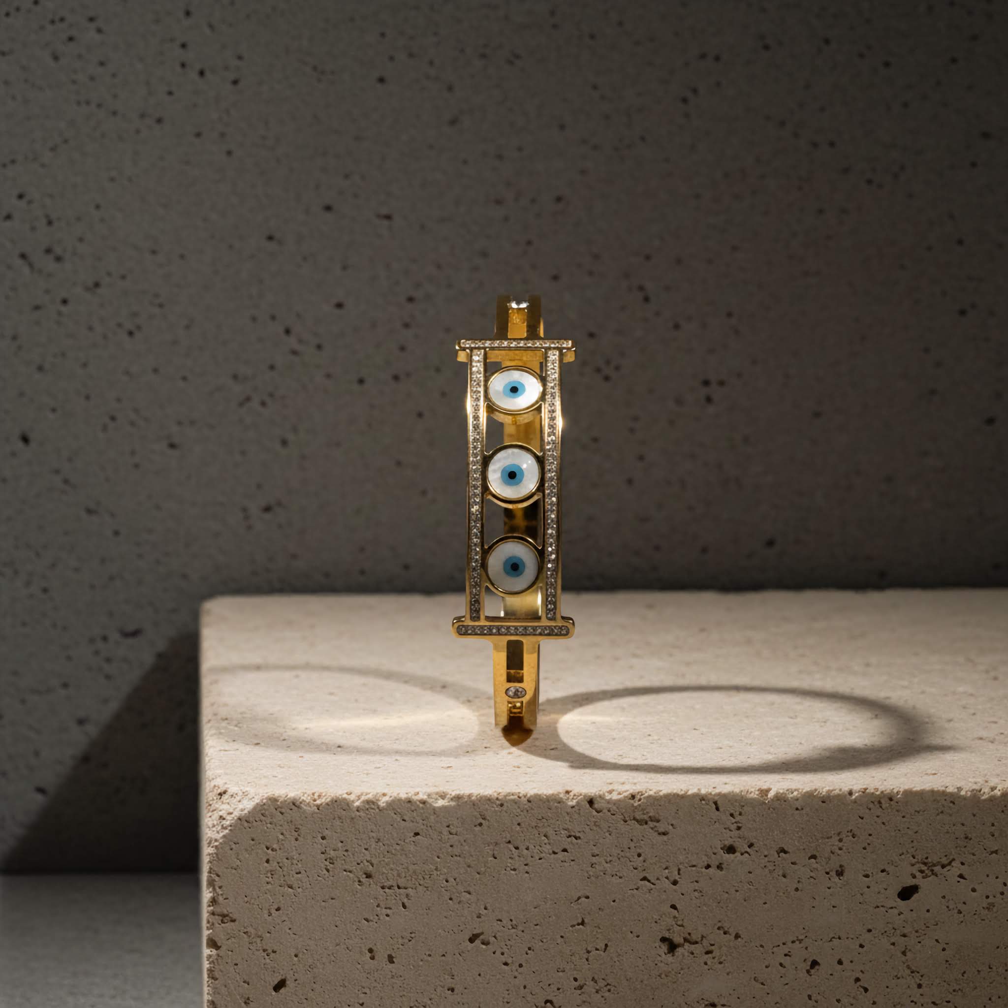 18k Gold plated bracelet with three evil eye shaped stones on a concrete surface and dark background