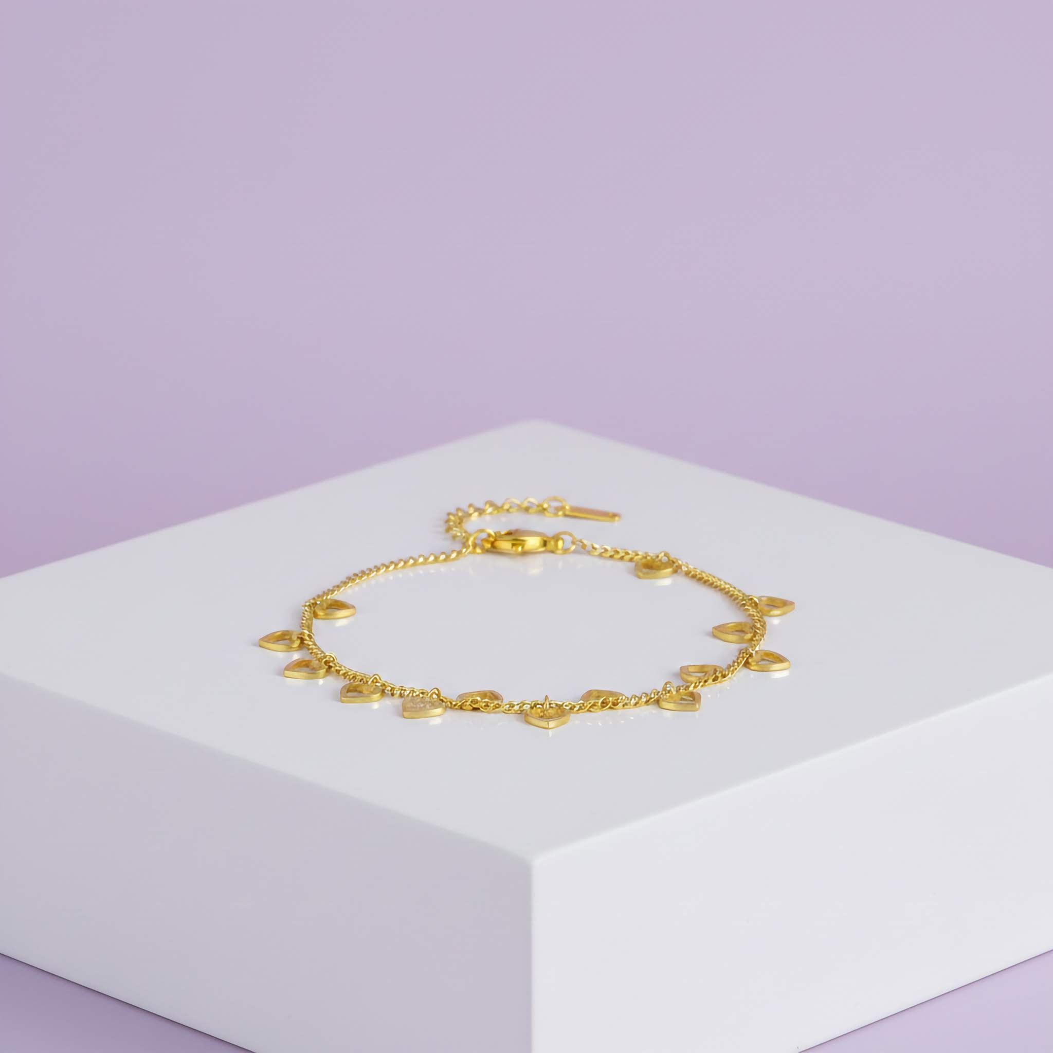 18k Gold plated mini heart bracelet on a white stand with a light purple background