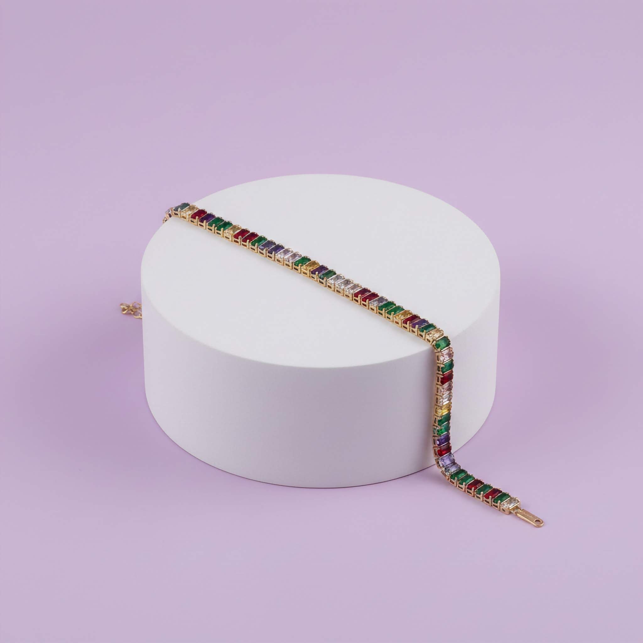 Multicoloured gemstone bracelet on a white cylindrical stand against a light purple background