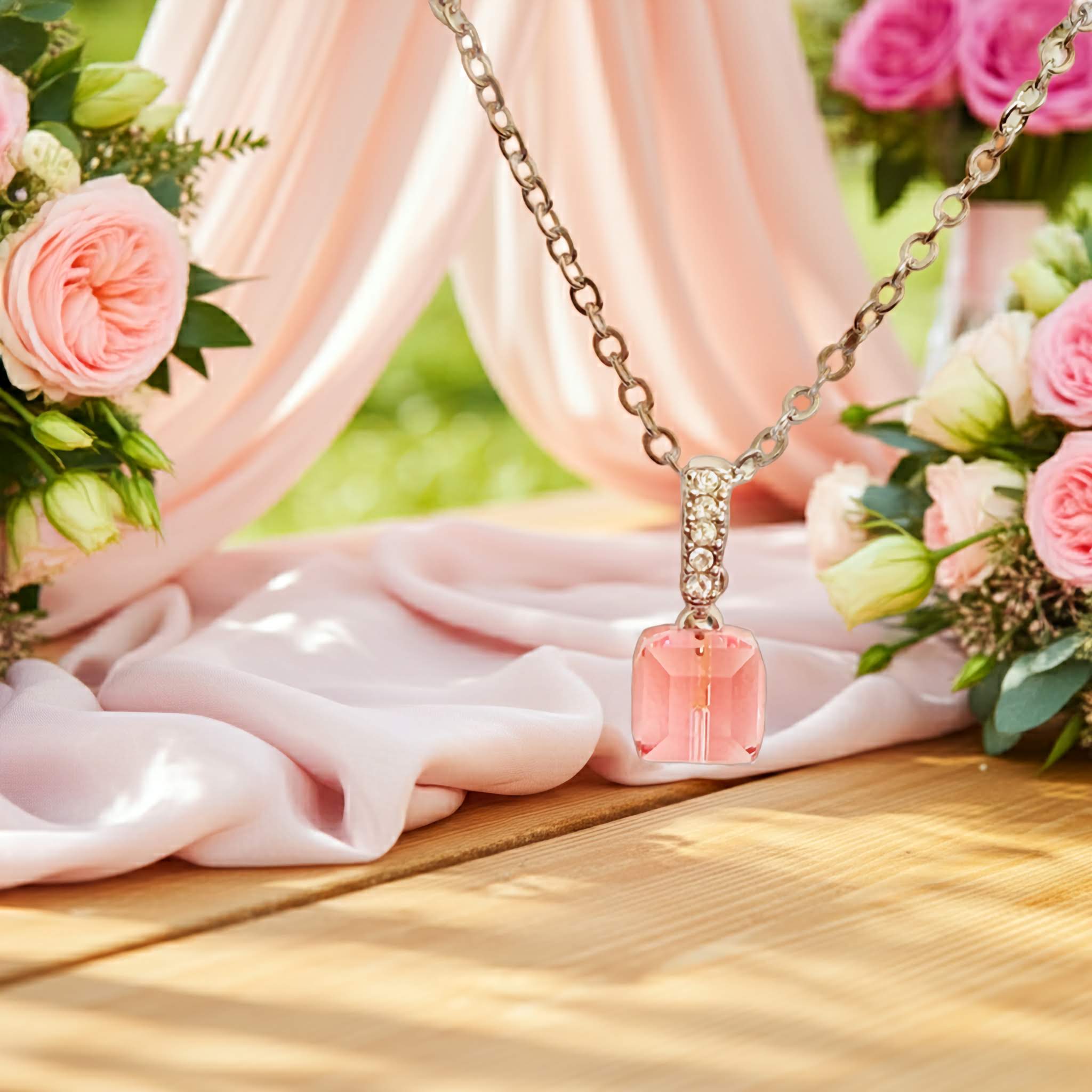 18k gold plated Necklace with a pink radiant cut pendant on a wooden surface with flowers in the background