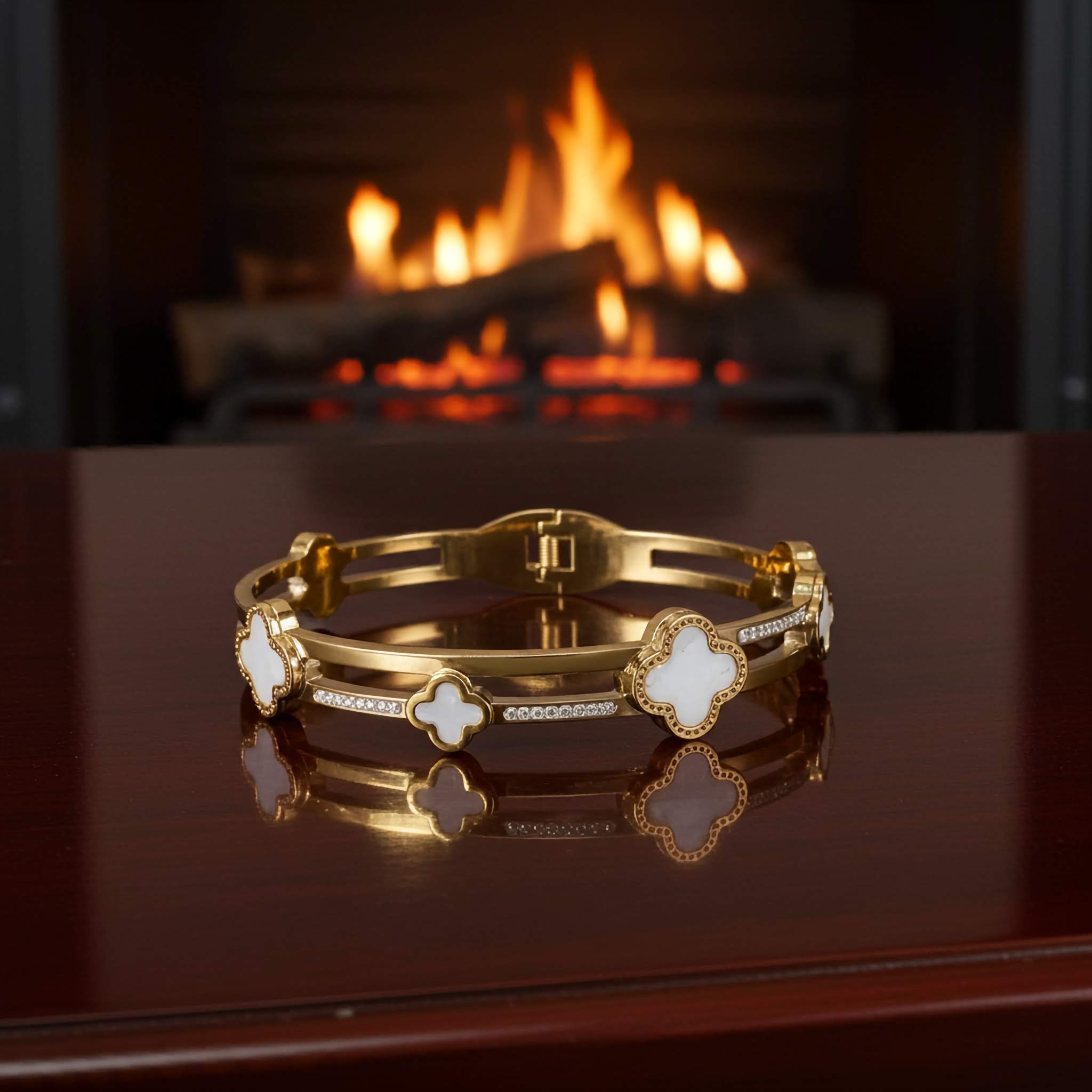 Gold clover bracelet with white stones on a reflective surface in front of a fireplace