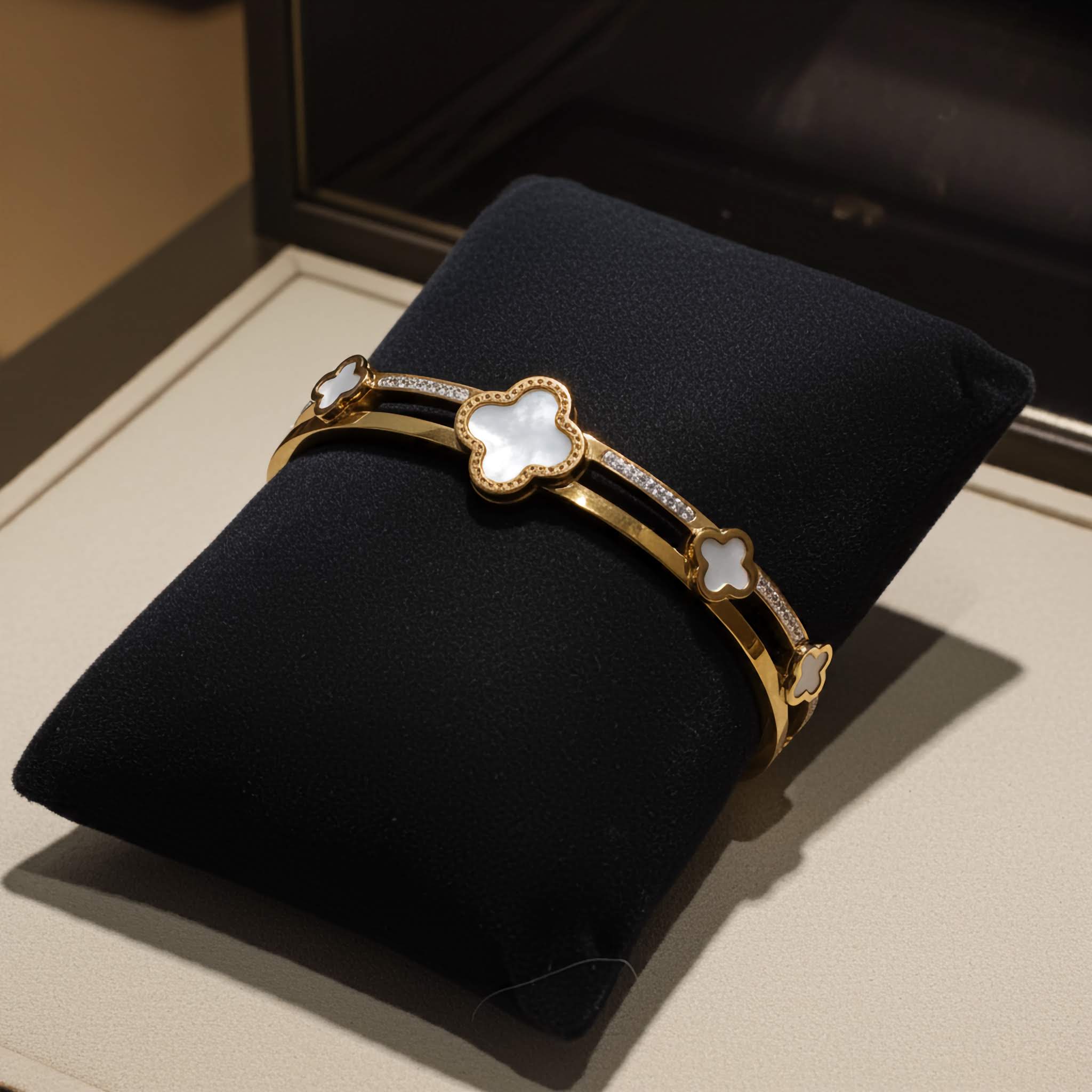 Buy Gold clover bracelet with white stones on a black cushion against a beige background