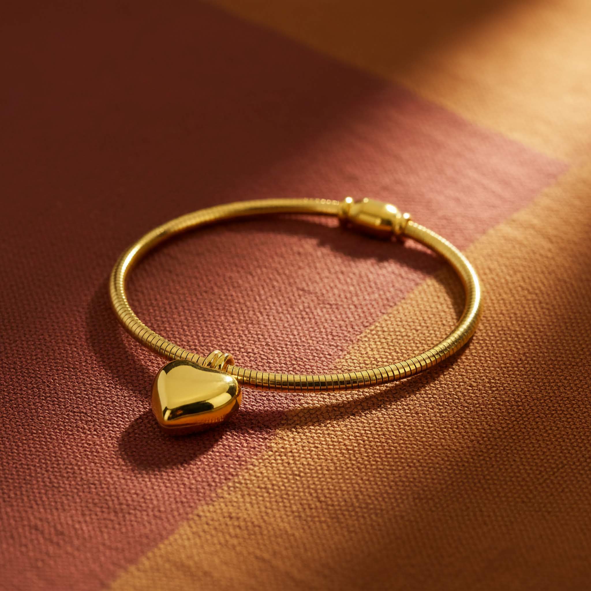 A 18k Gold plated bracelet with a heart-shaped charm on a textured brown surface