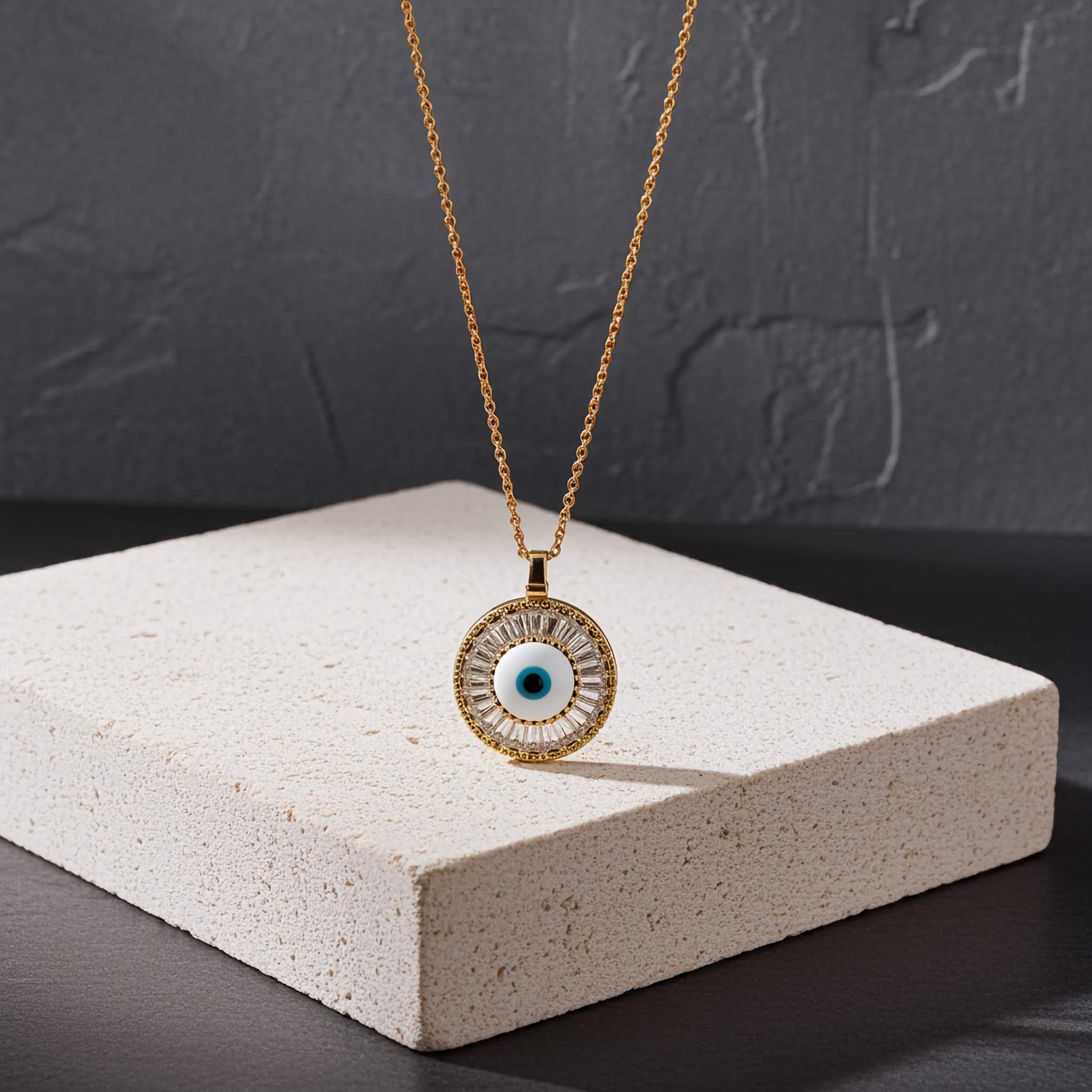 A Gold necklace with an eye-shaped pendant on a white block against a dark background