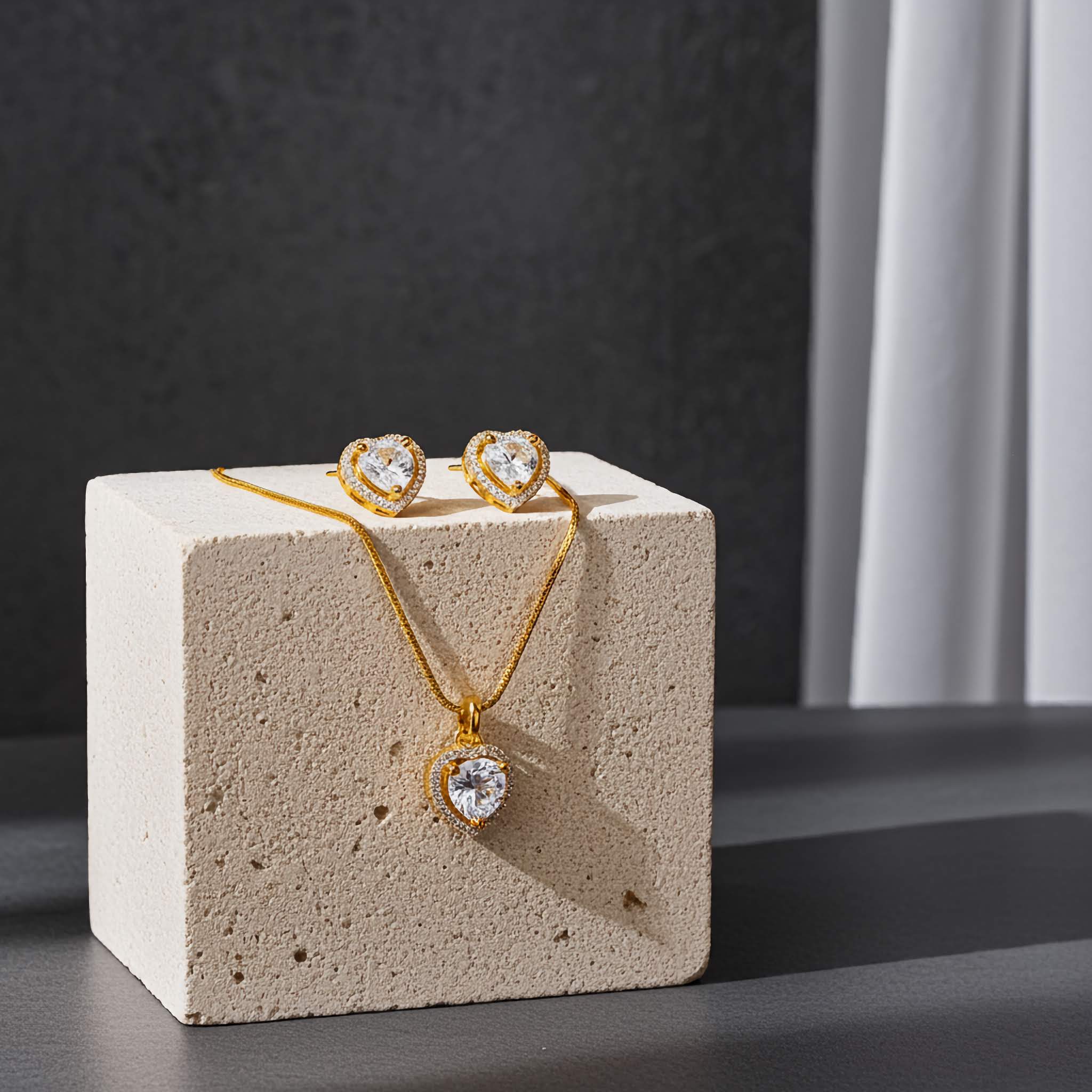 18k Gold plated zironia diamond necklace and heart-shaped earrings on a textured beige stand with a dark background