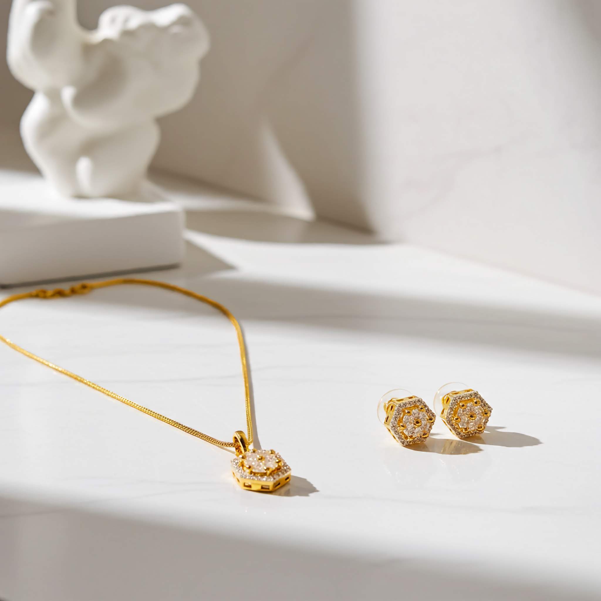Zirconia set of 18k Gold plated necklace and earrings on a light surface with a white elephant sculpture in the background.