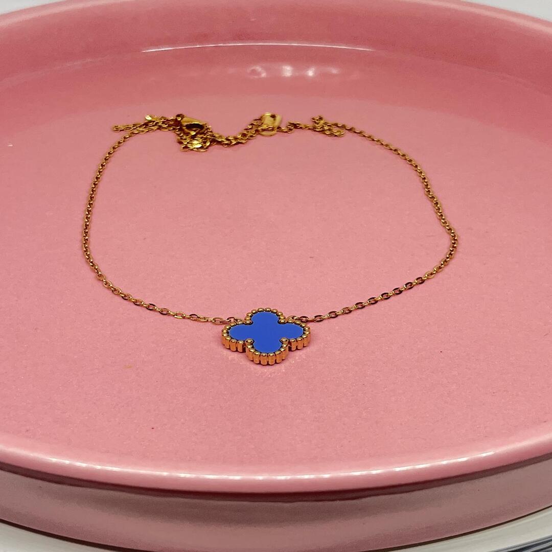 Gold chain with a blue clover charm on a pink plate