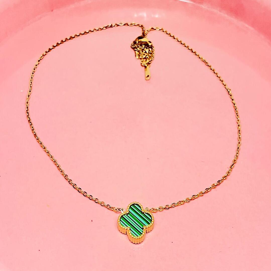Gold necklace with a green clover-shaped charm on a pink background