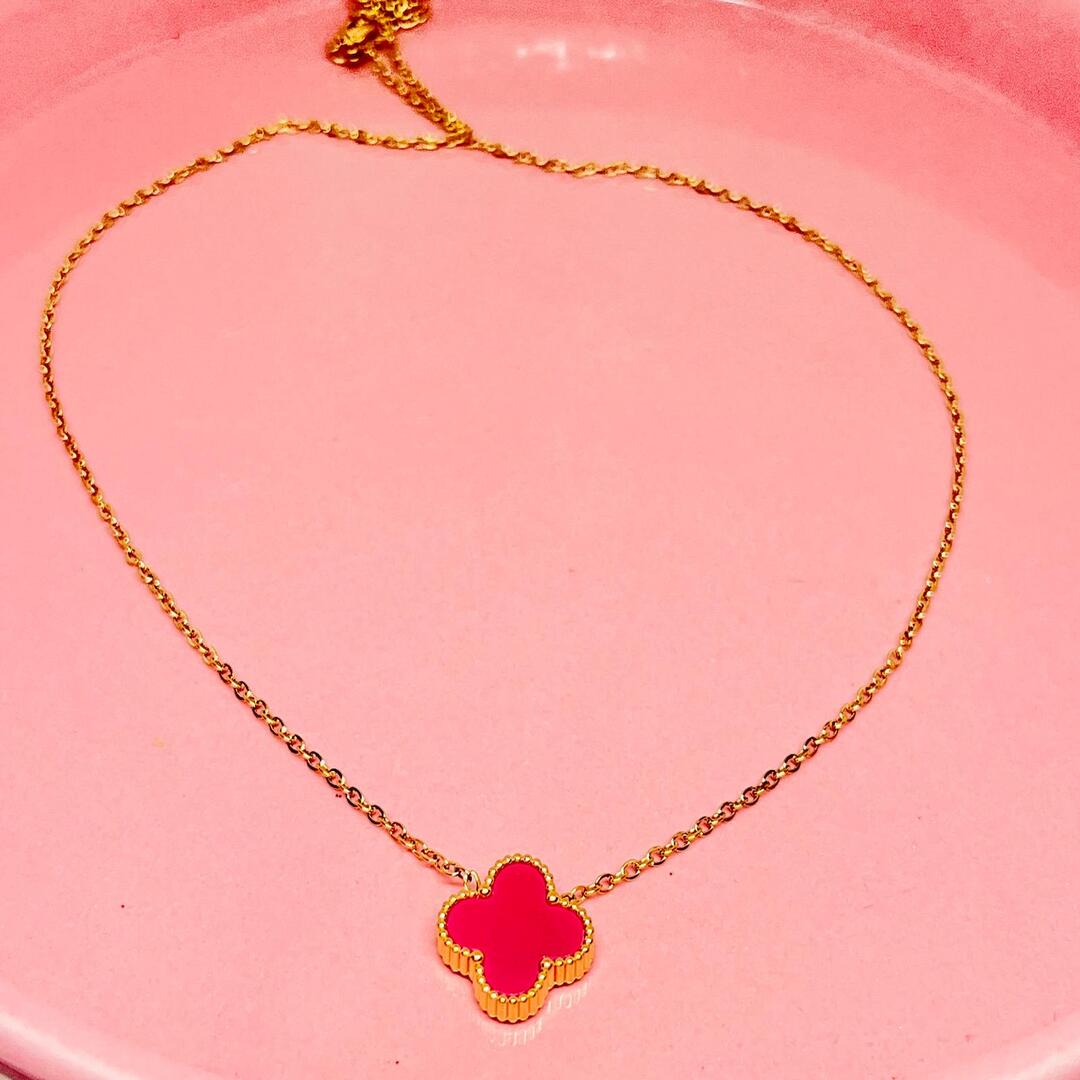 Gold necklace with a red clover pendant on a pink heart-shaped background
