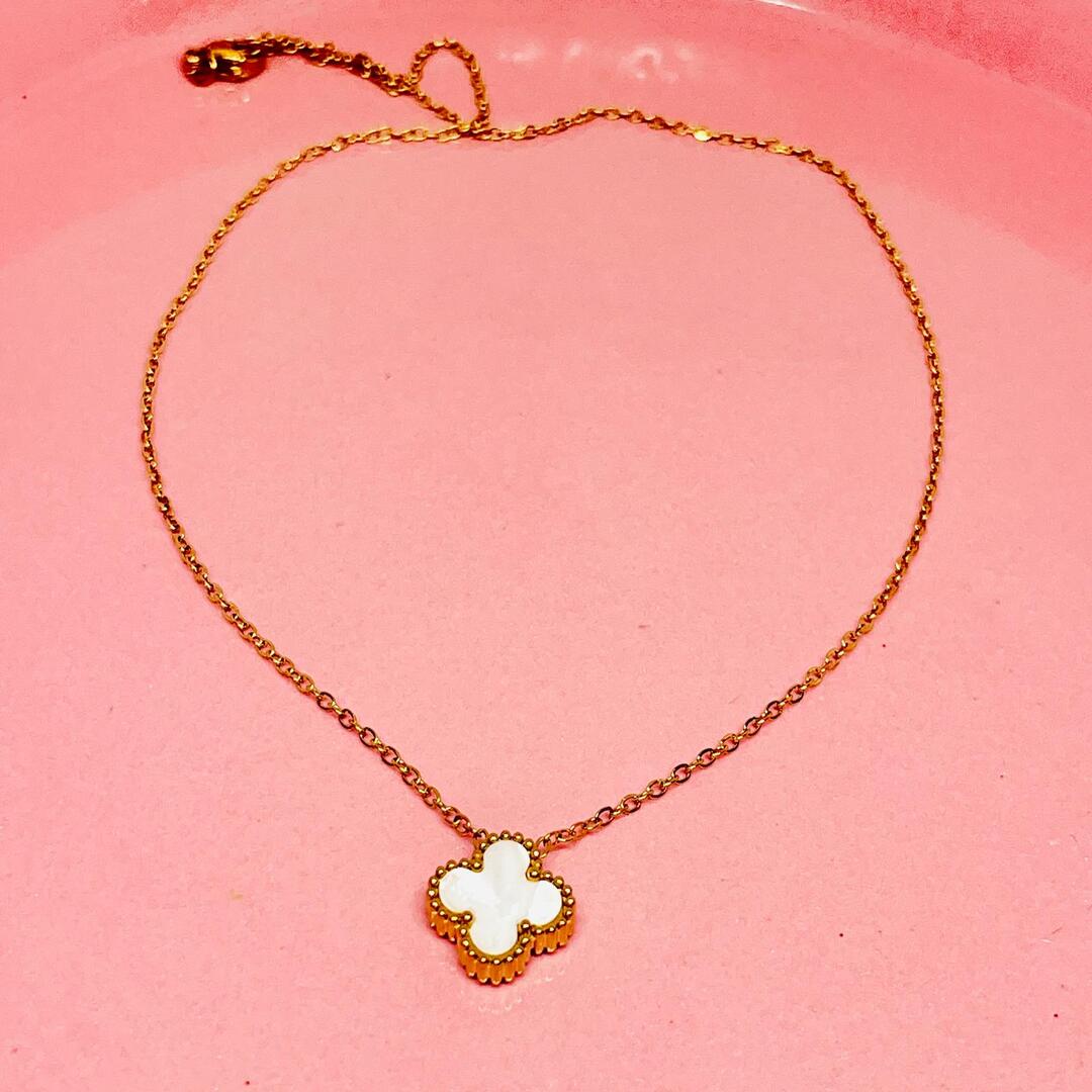 Gold necklace with a clover-shaped pendant on a pink background