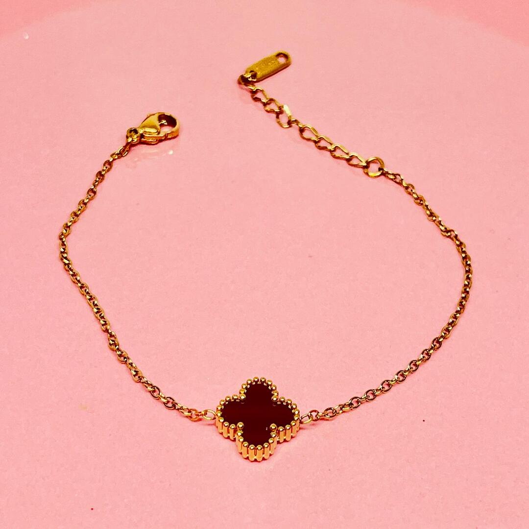 Gold necklace with a clover-shaped black stone on a pink background