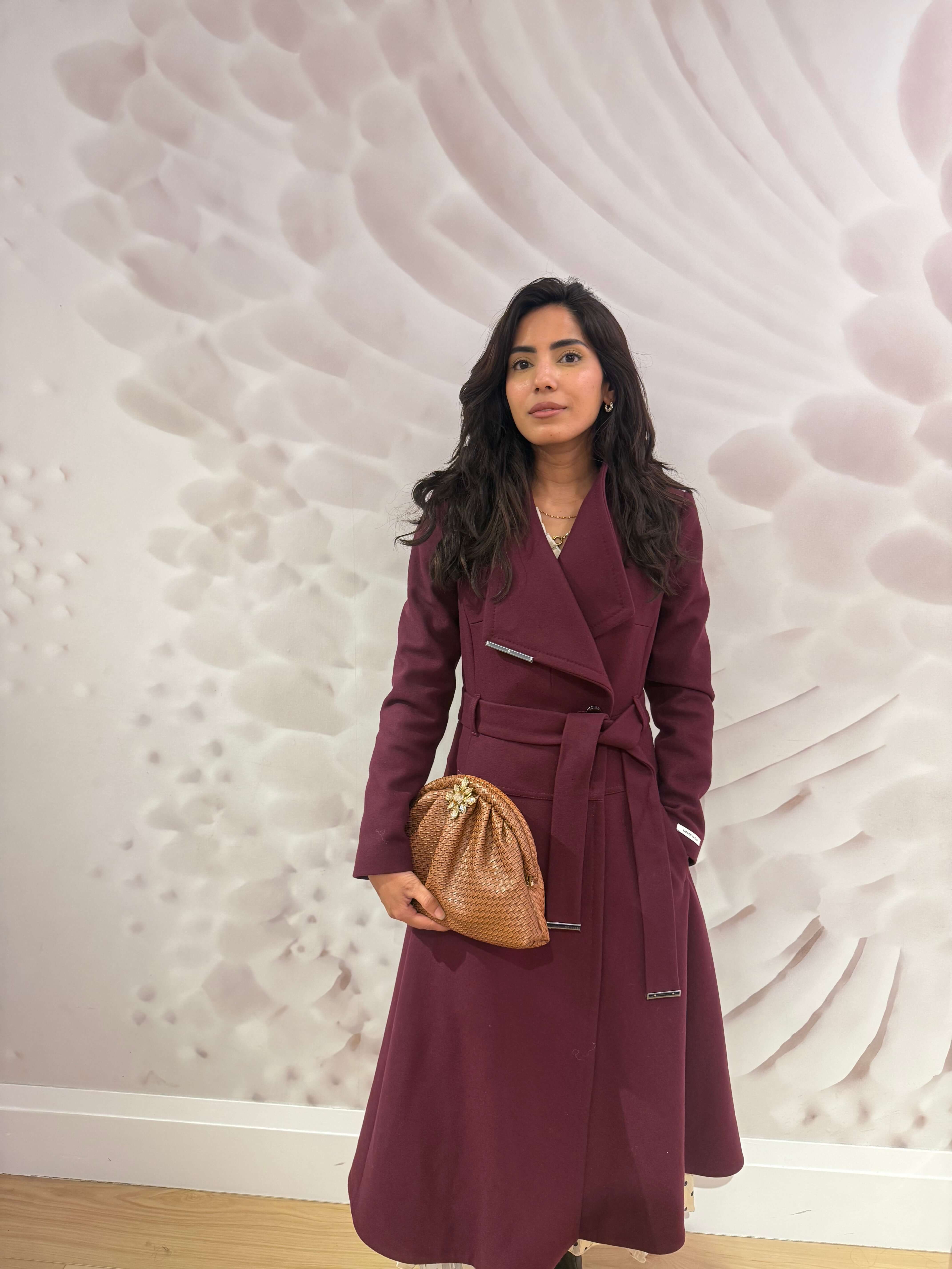 Model wearing a maroon coat holding The Luxe Weave Clutch, featuring a textured design and elegant embellishments.