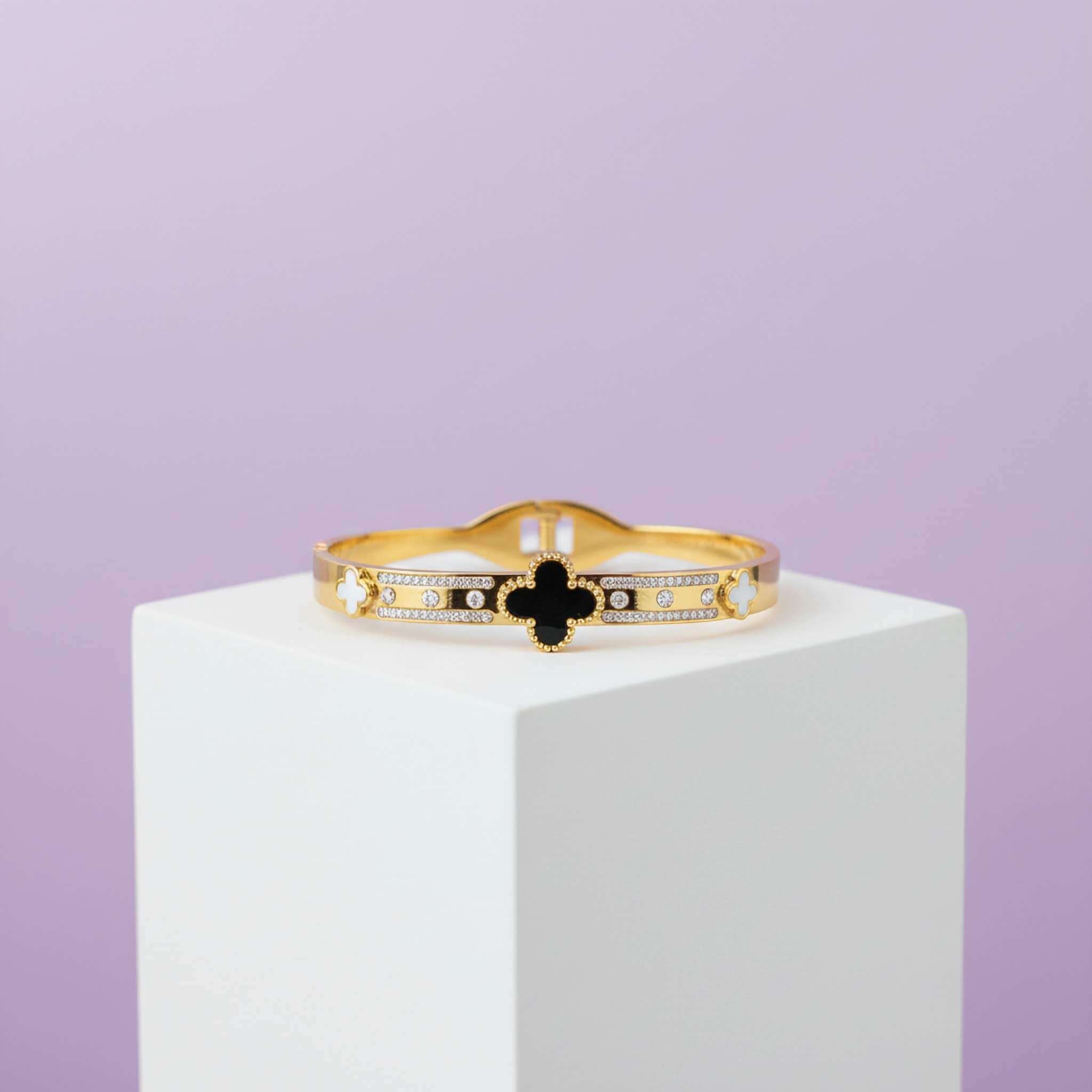 Black and white clover leaf bracelet on a white stand and purple background