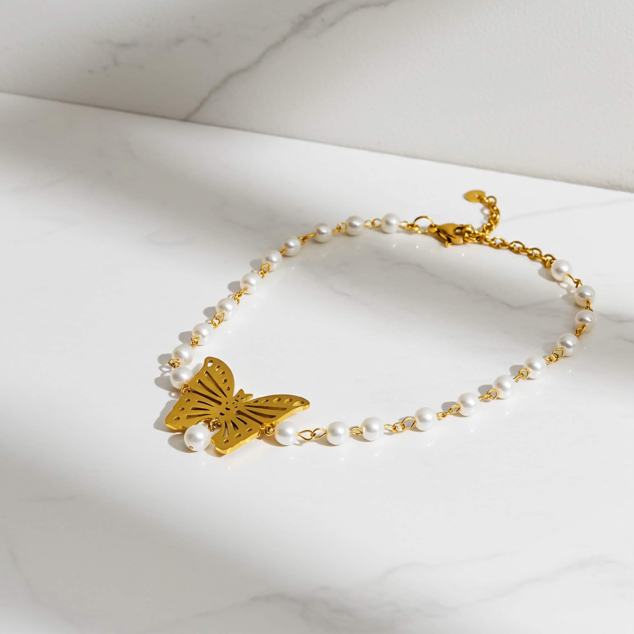 Gold butterfly necklace with pearl beads on a marble surface