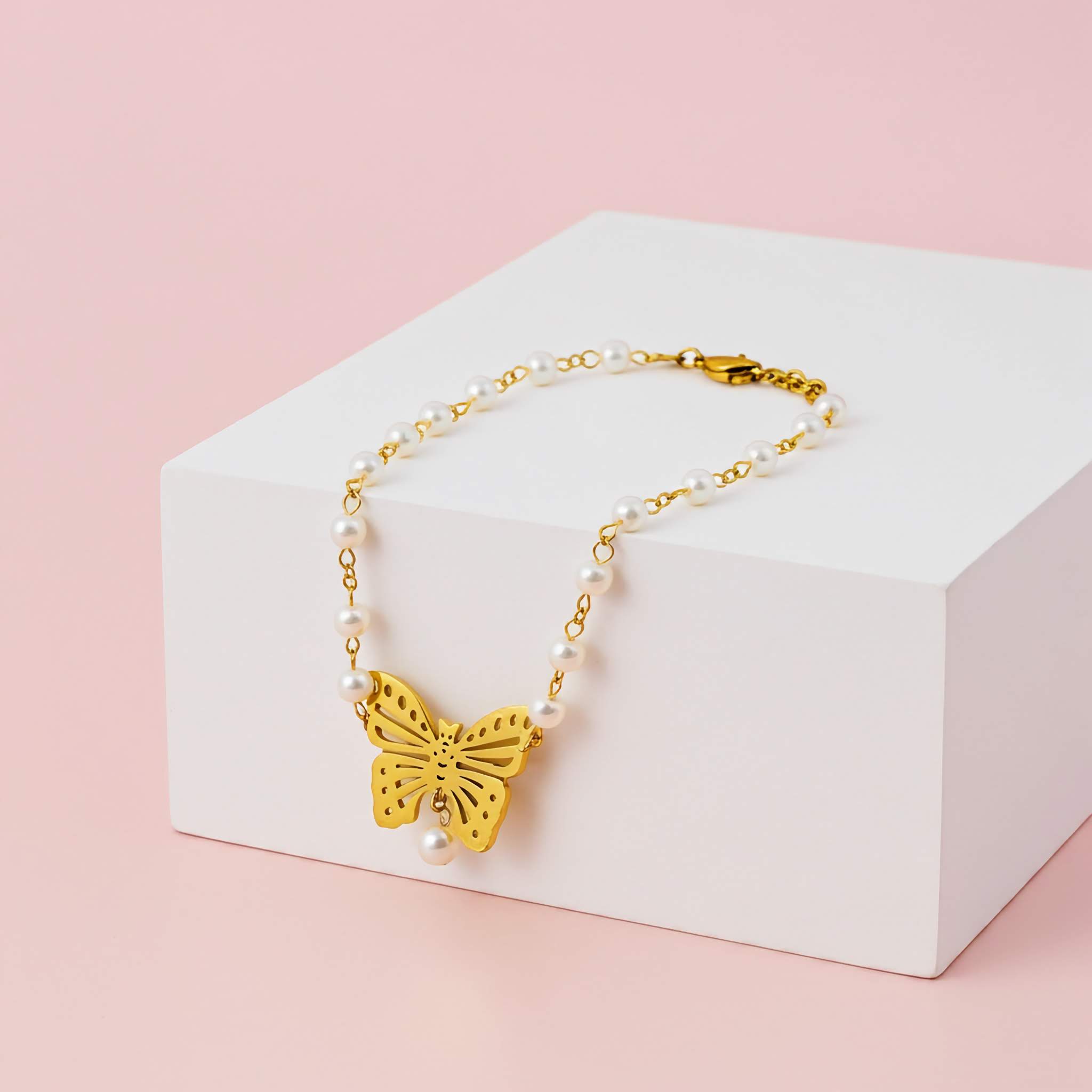 Gold butterfly necklace with pearls on a white box against a pink background