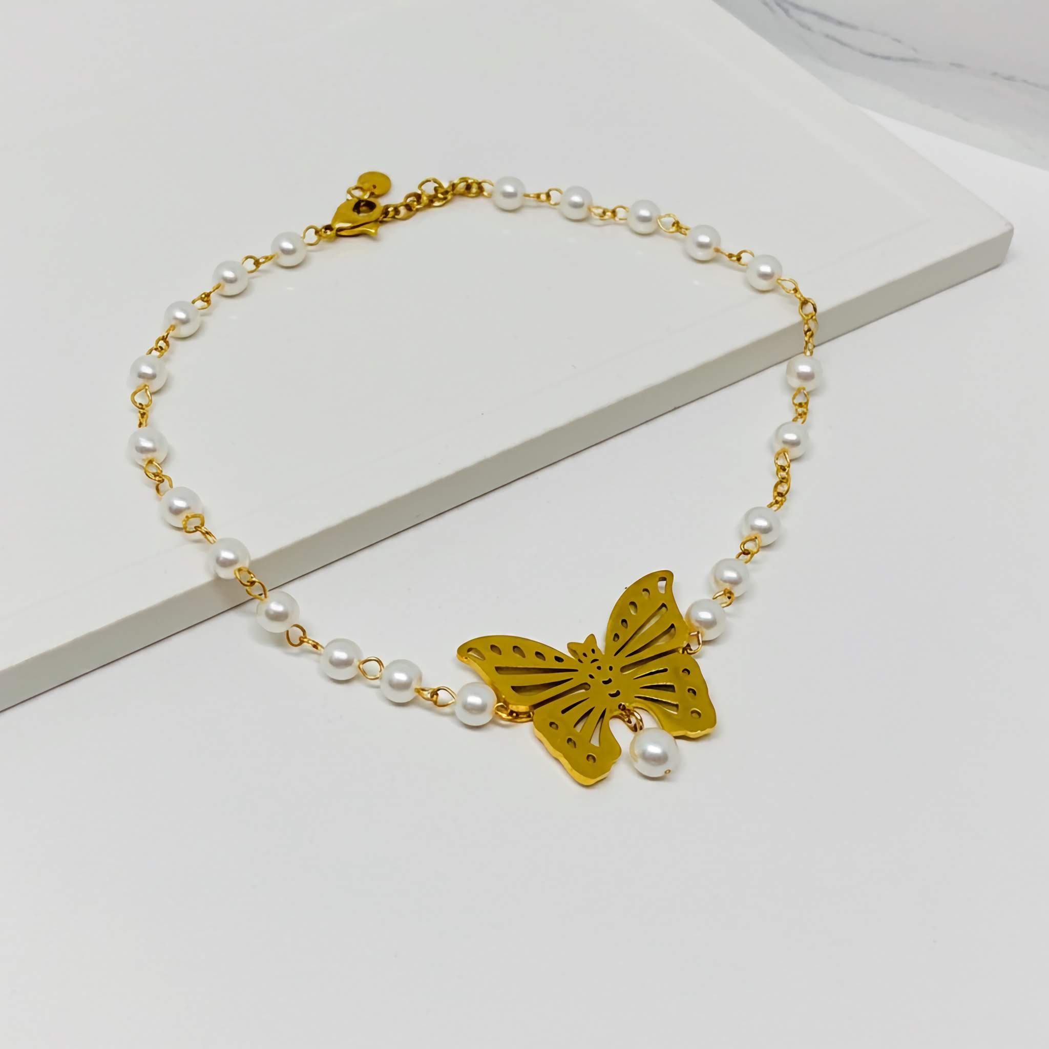 Necklace with gold butterfly charm and pearl beads on a white surface