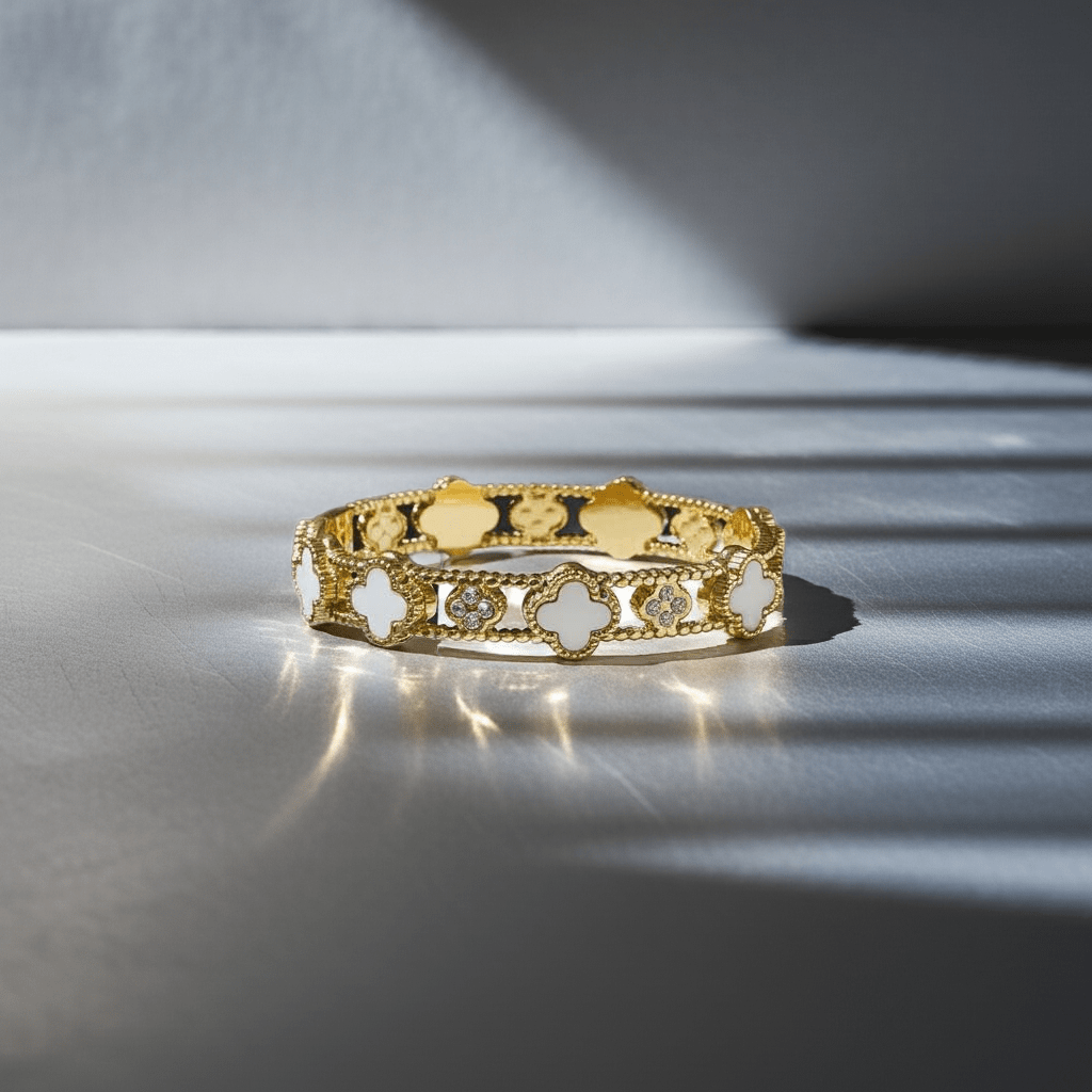 Gold plated 4 leaf white clover bangle on a grey surface,