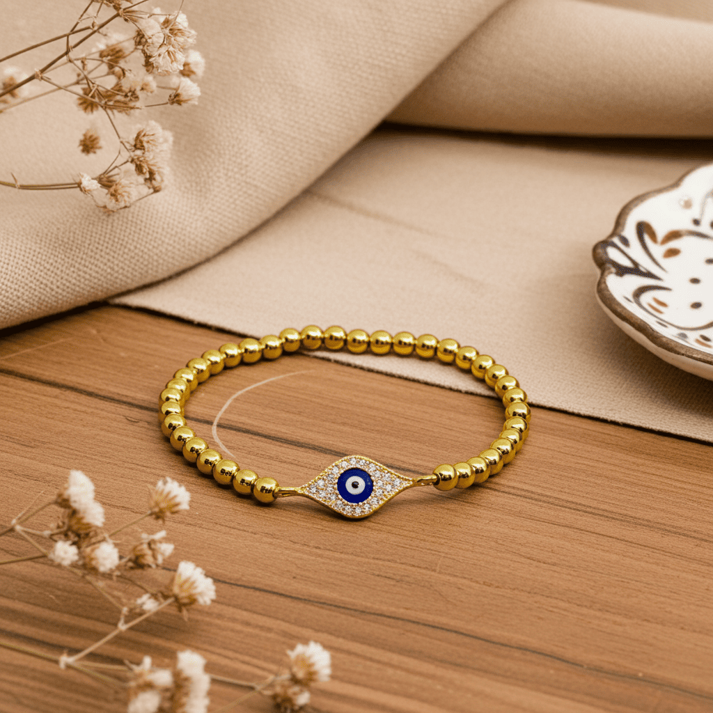 buy evil eye Gold slip-on bracelet with a blue evil eye charm on a wooden surface with dried flowers.