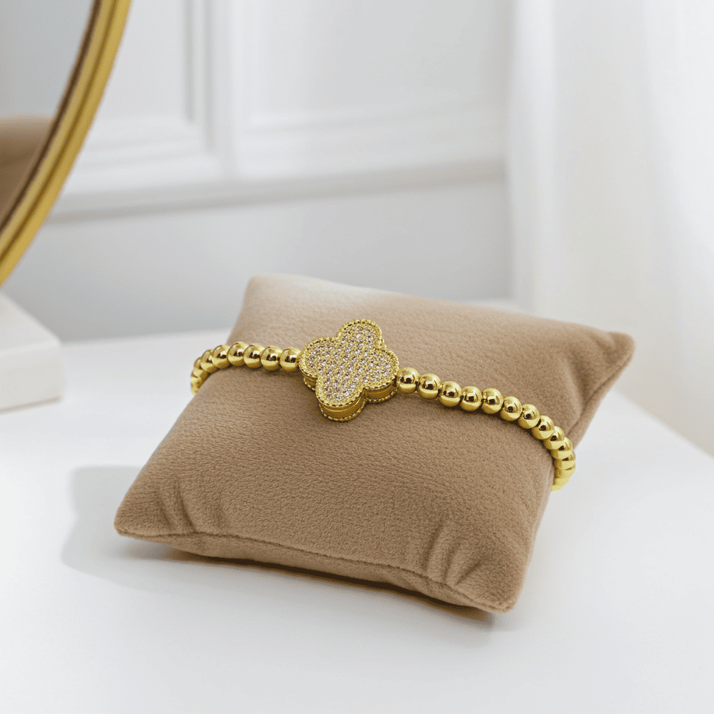 Gold slip on bracelet with a cloveron a beige pillow against a white background