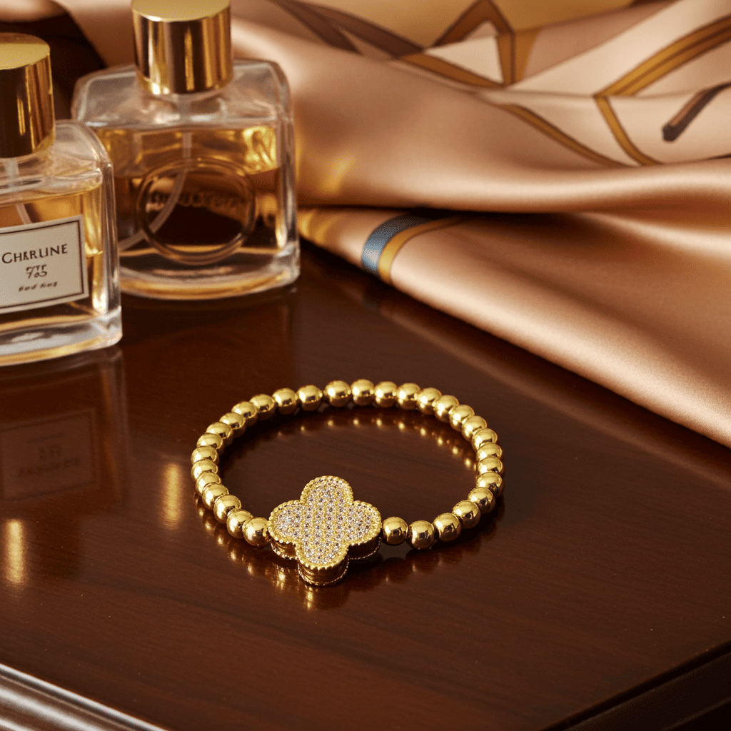 Gold slip-on bracelet with clover design on a reflective surface next to two perfume bottles.