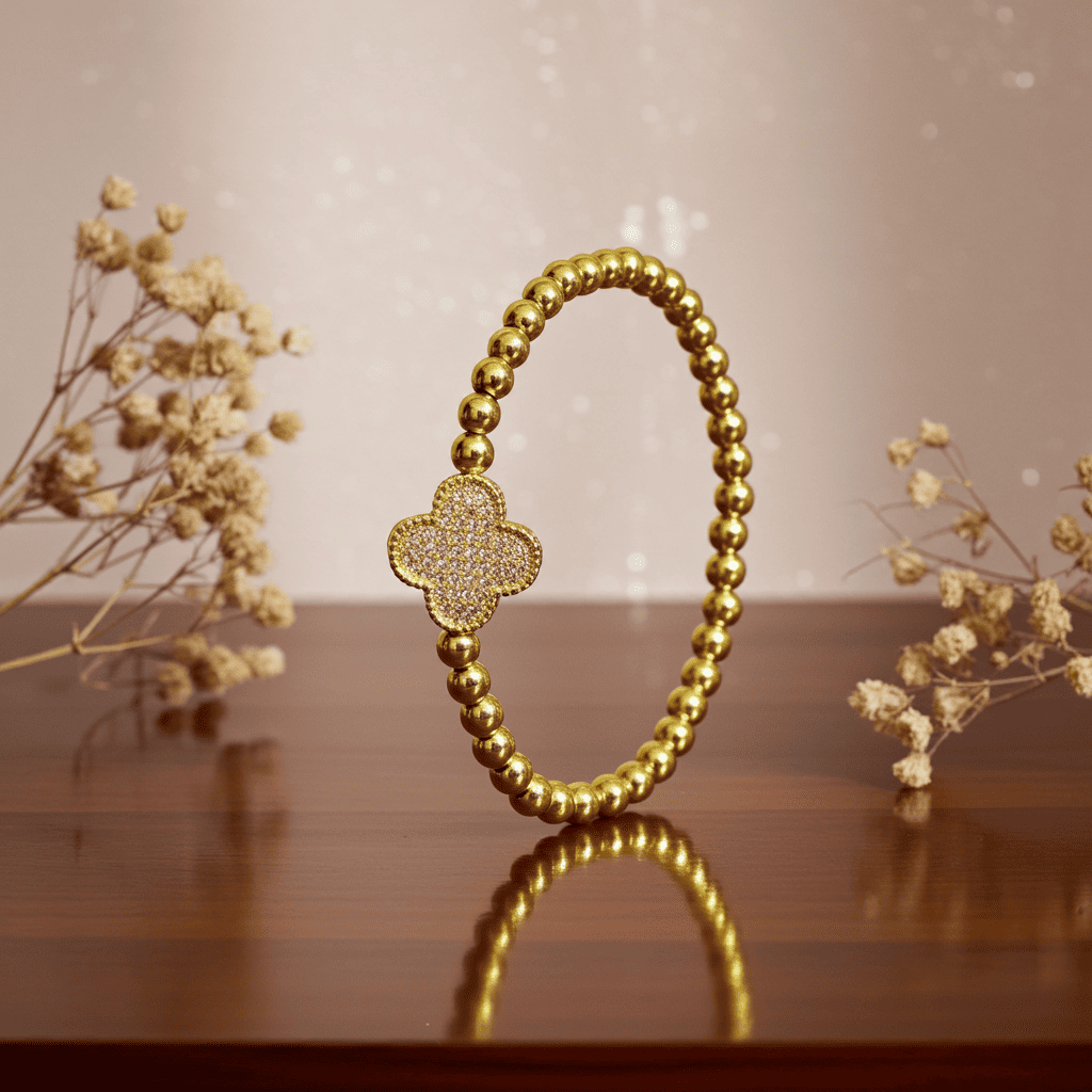 Buy Slip-on Gold bracelet with clover charm on a reflective surface with dried flowers in the background