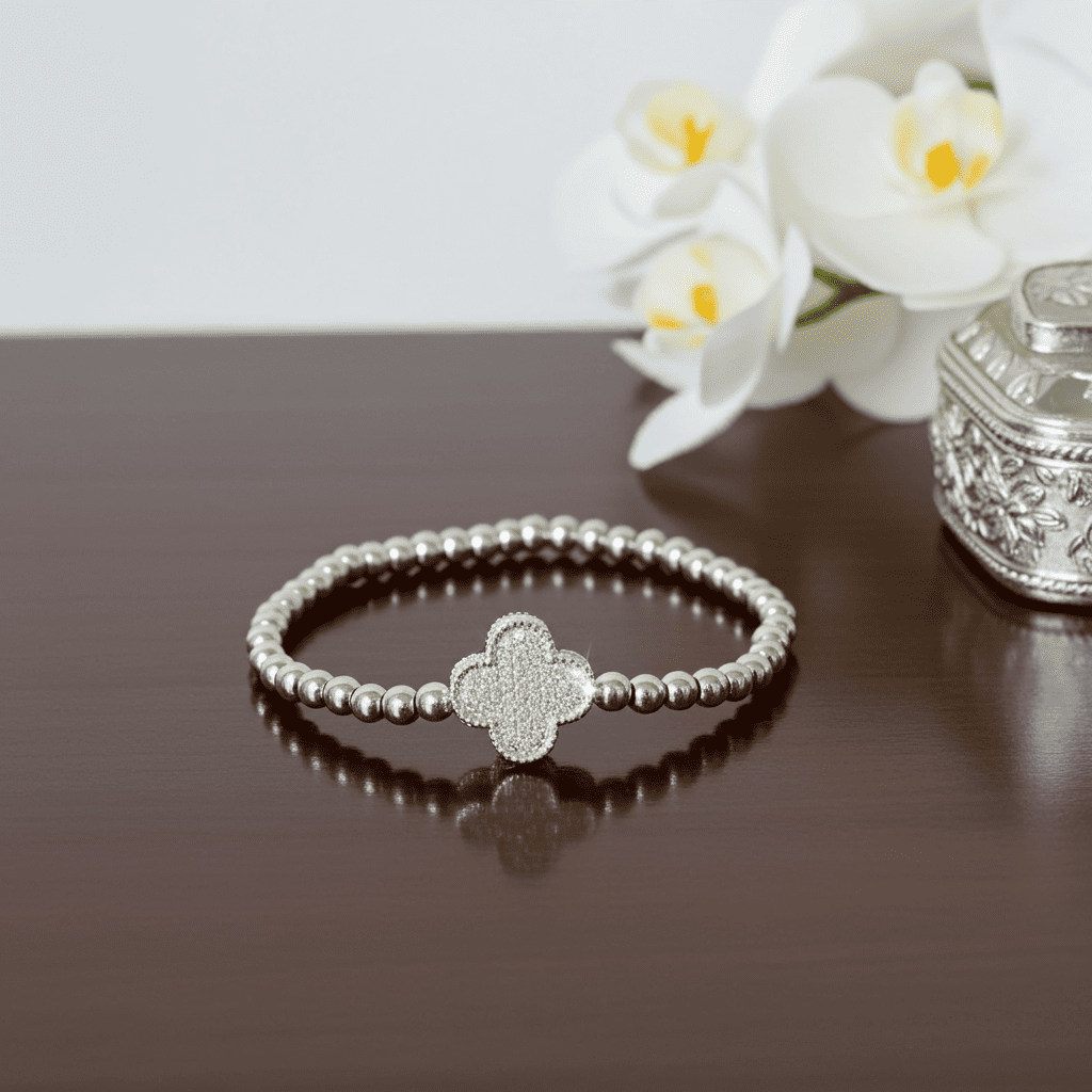 Silver slip-on bracelet with clover charm on a wooden surface with white flowers in the background
