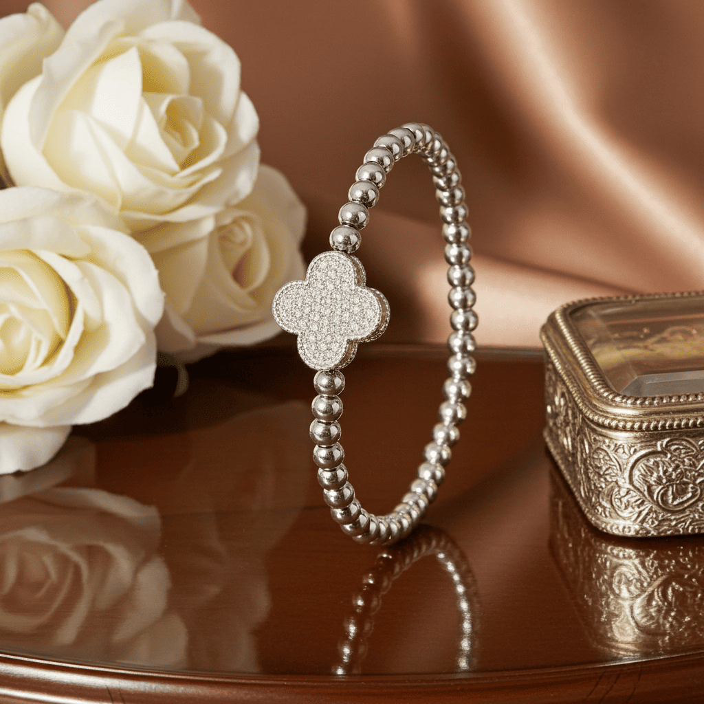 Buy Silver slip on bracelet with clover charm on a reflective surface with white roses and an ornate box.