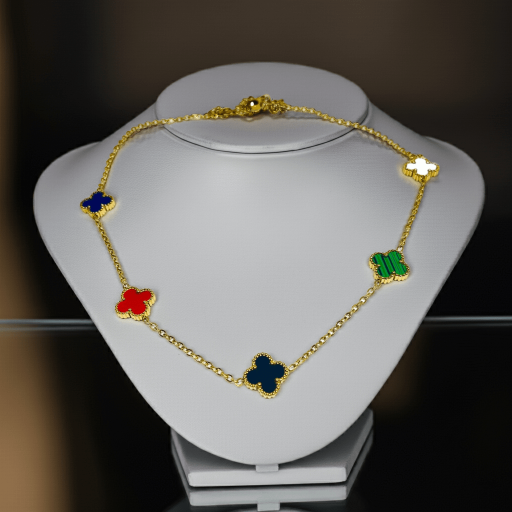 Gold necklace with colorful flower pendants on a white stand against a dark background