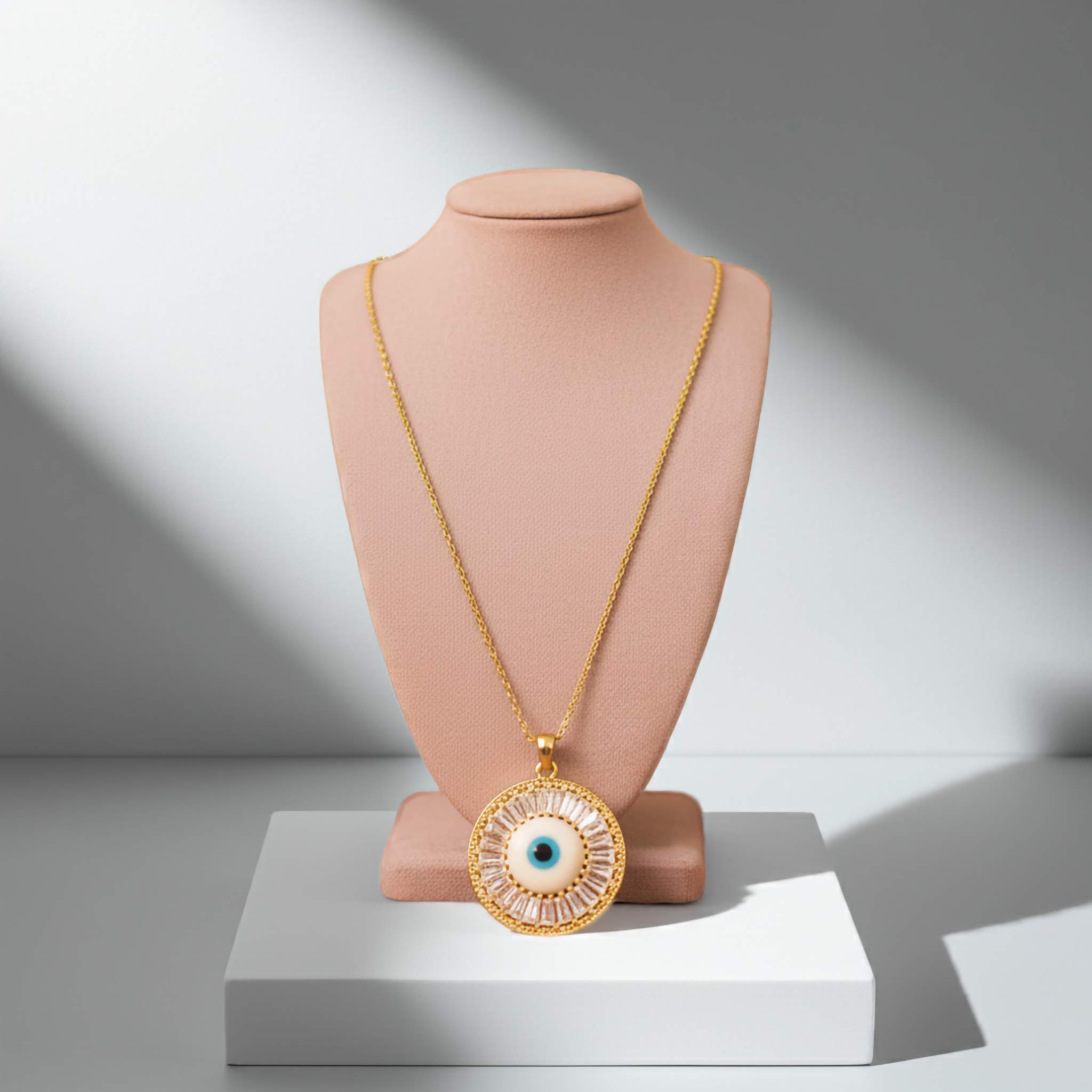 Gold necklace with an eye-shaped pendant on a mannequin bust against a neutral background