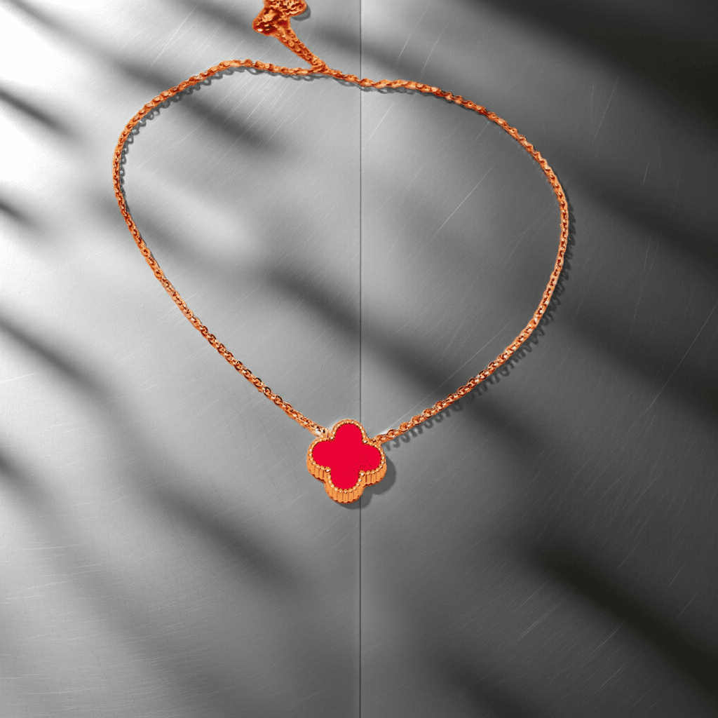 Gold Necklace with a red clover pendant on an orange cord against a gray background