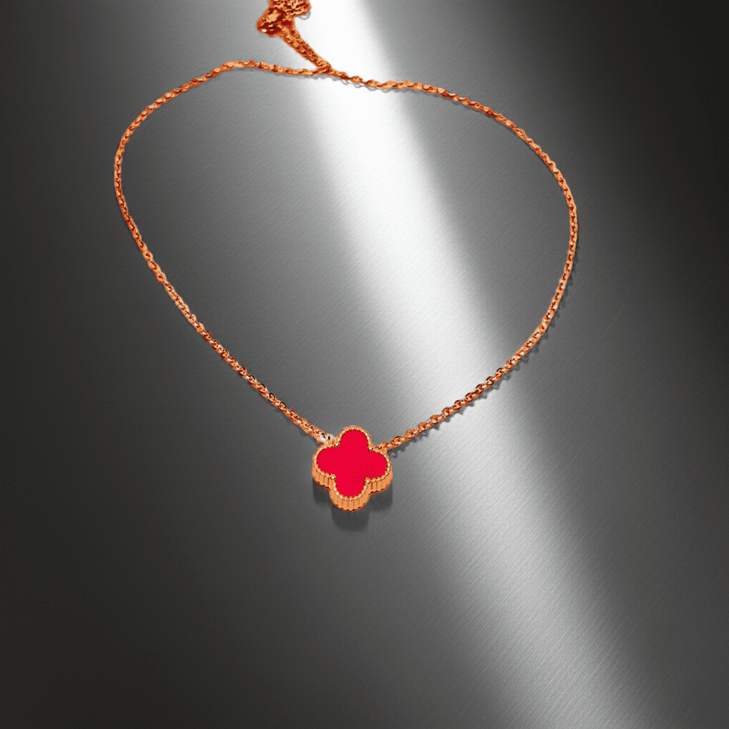 Gold Necklace with a red clover pendant on a reflective gray surface