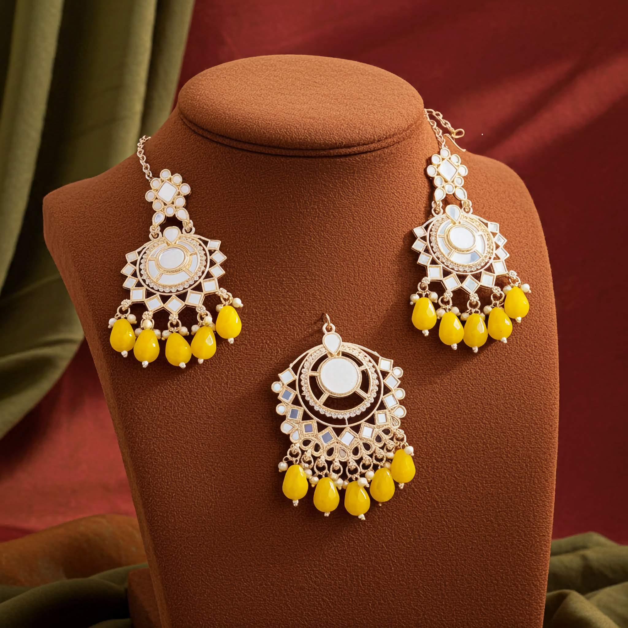 Glass work Gold and yellow jewelry set earrings and tikka on a brown mannequin bust with a red background