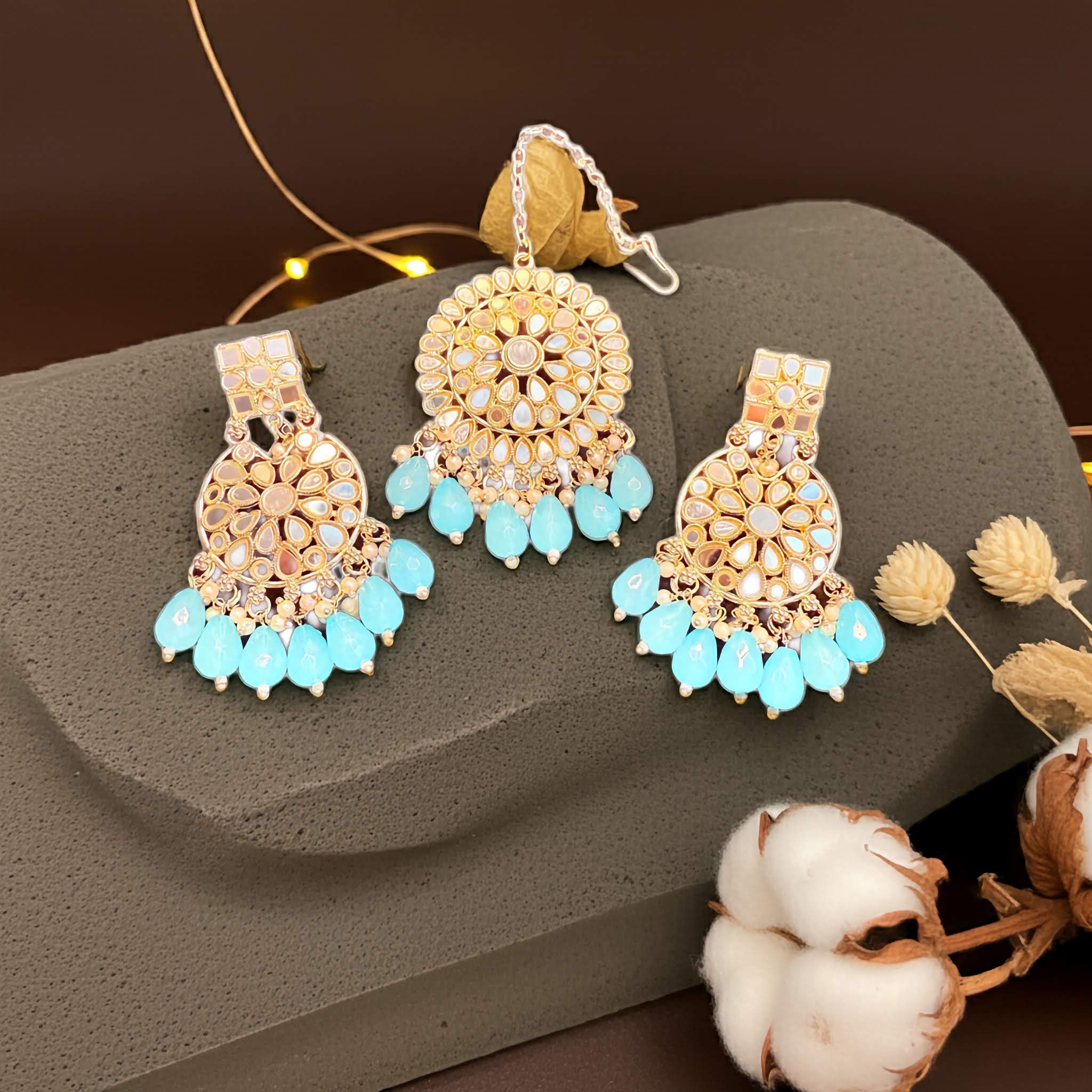 Gold and turquoise earrings and tikka set on a gray surface with decorative elements.