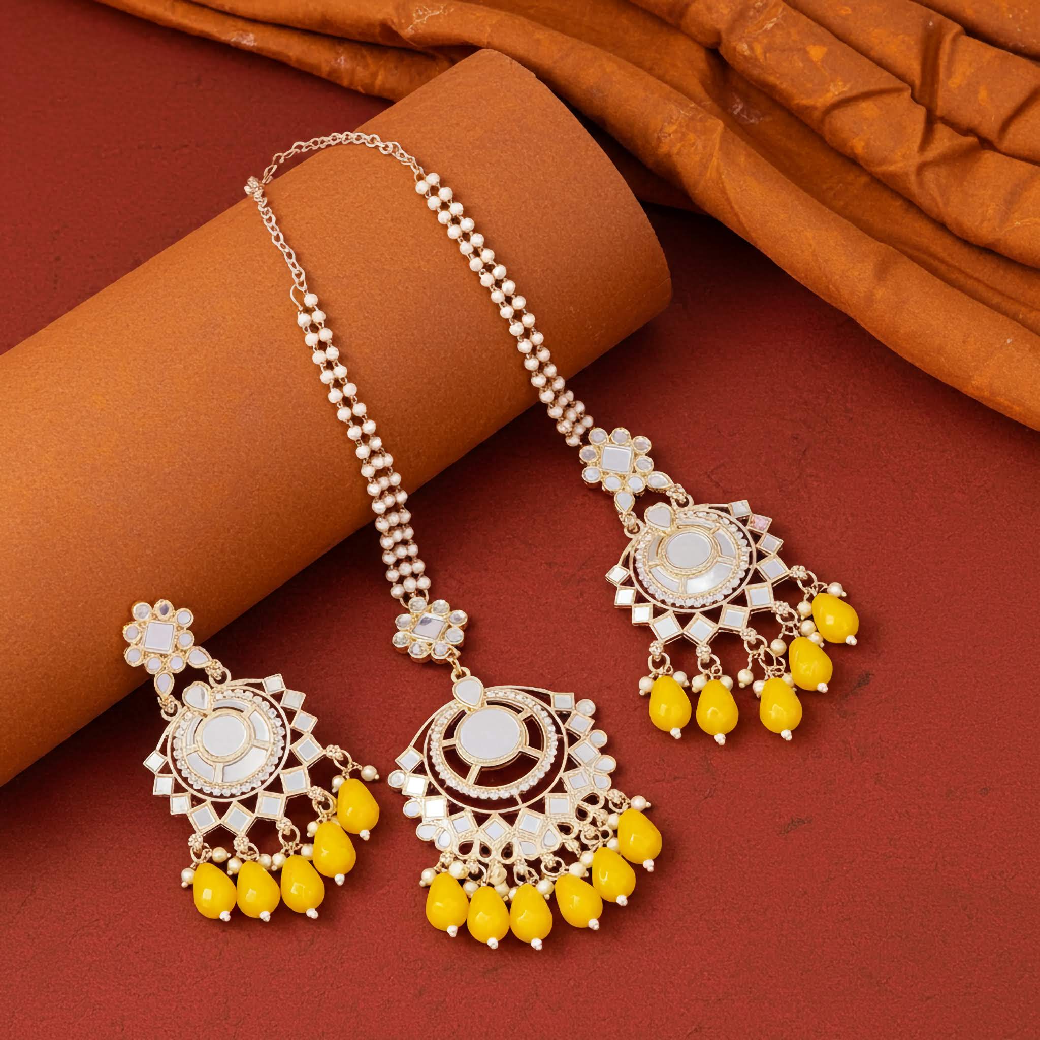 Gold and yellow Mirror earrings and tikka jewelry set on a brown fabric background
