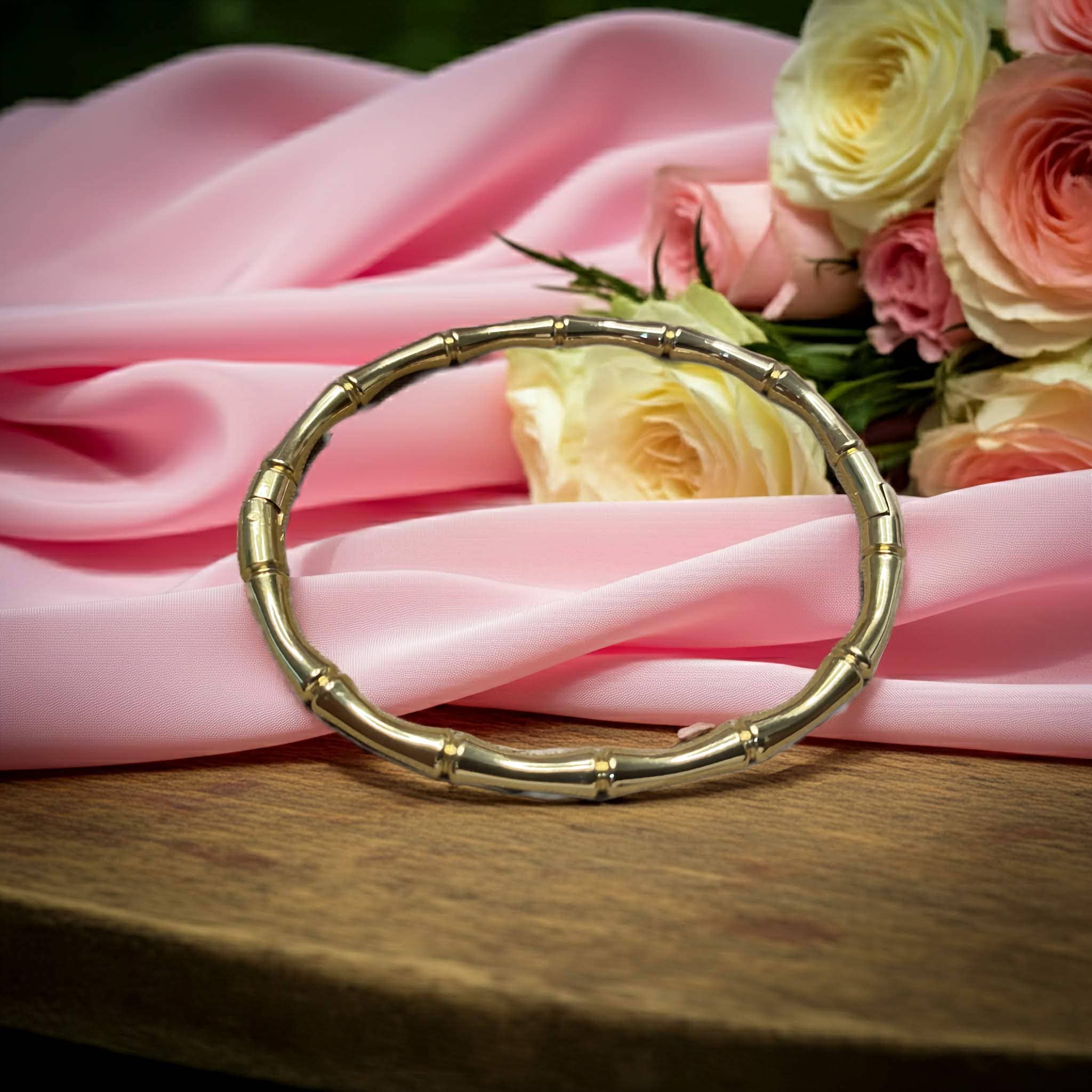 Gold bracelet on pink fabric with flowers in the background