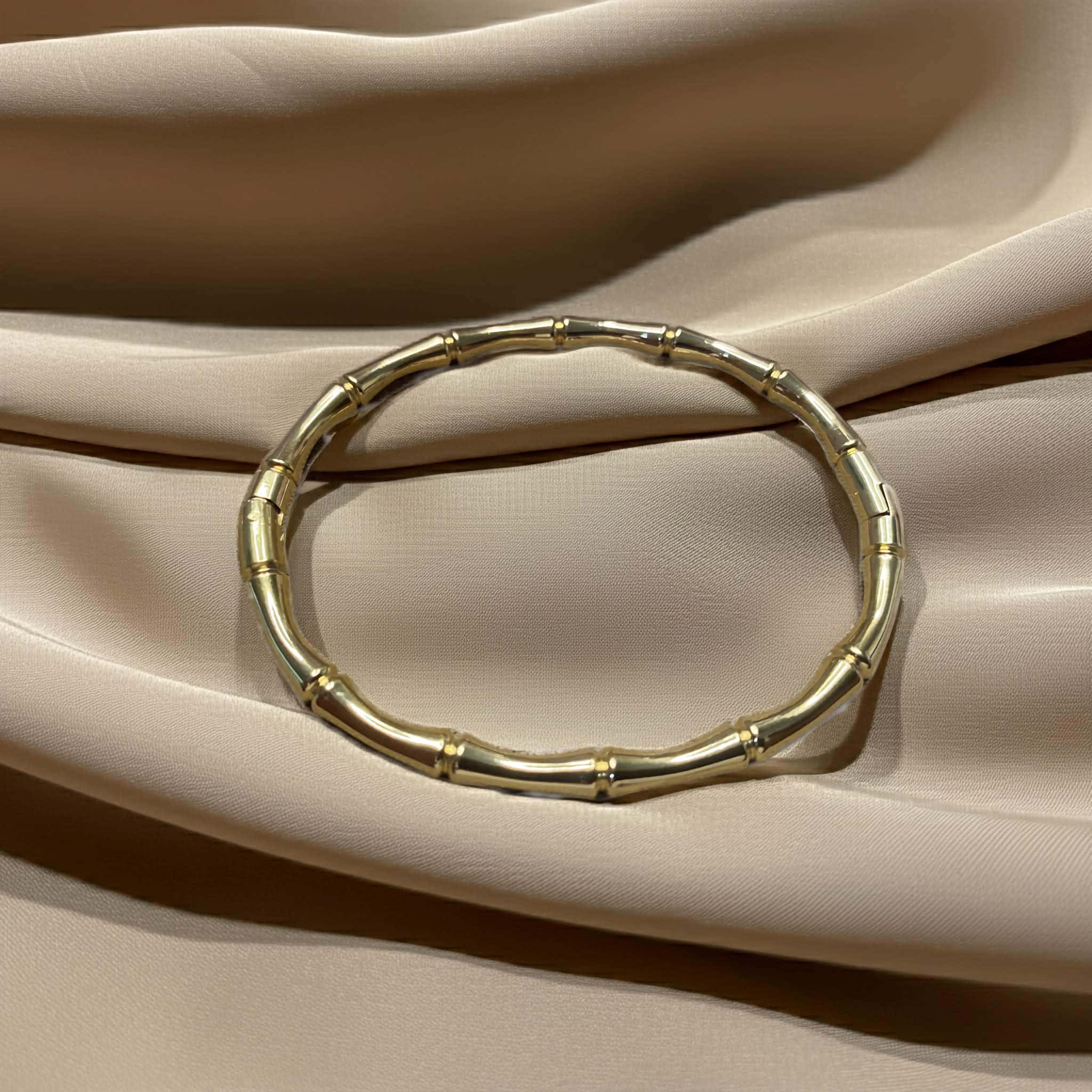 Gold bracelet bamboo style bangle on a beige fabric background