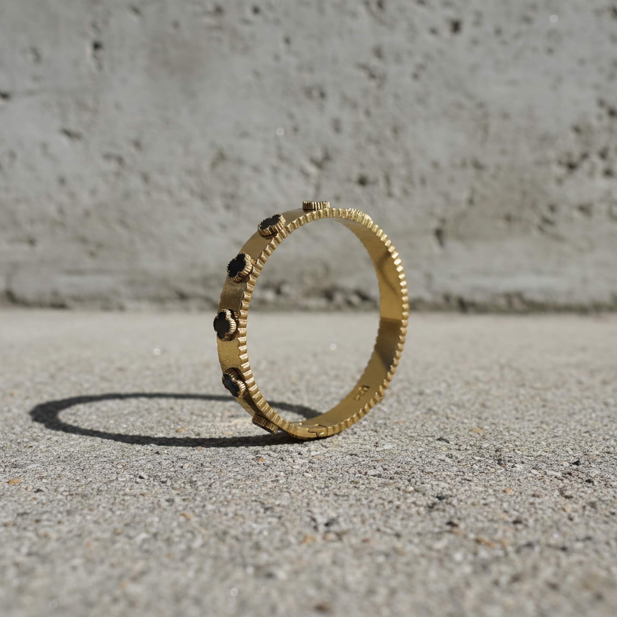 Gold bracelet with black clover leafs on a concrete surface