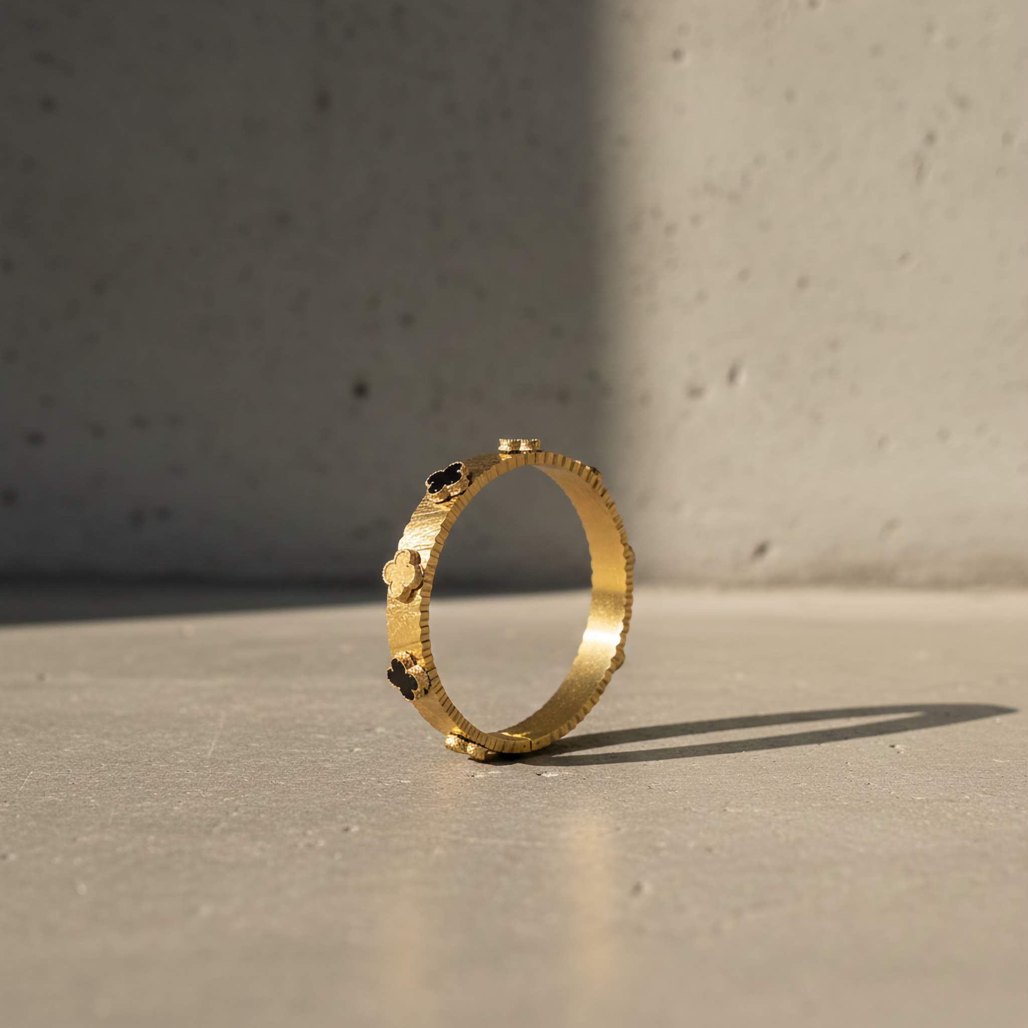 Gold bracelet with black/gold clover leafs design on a concrete surface