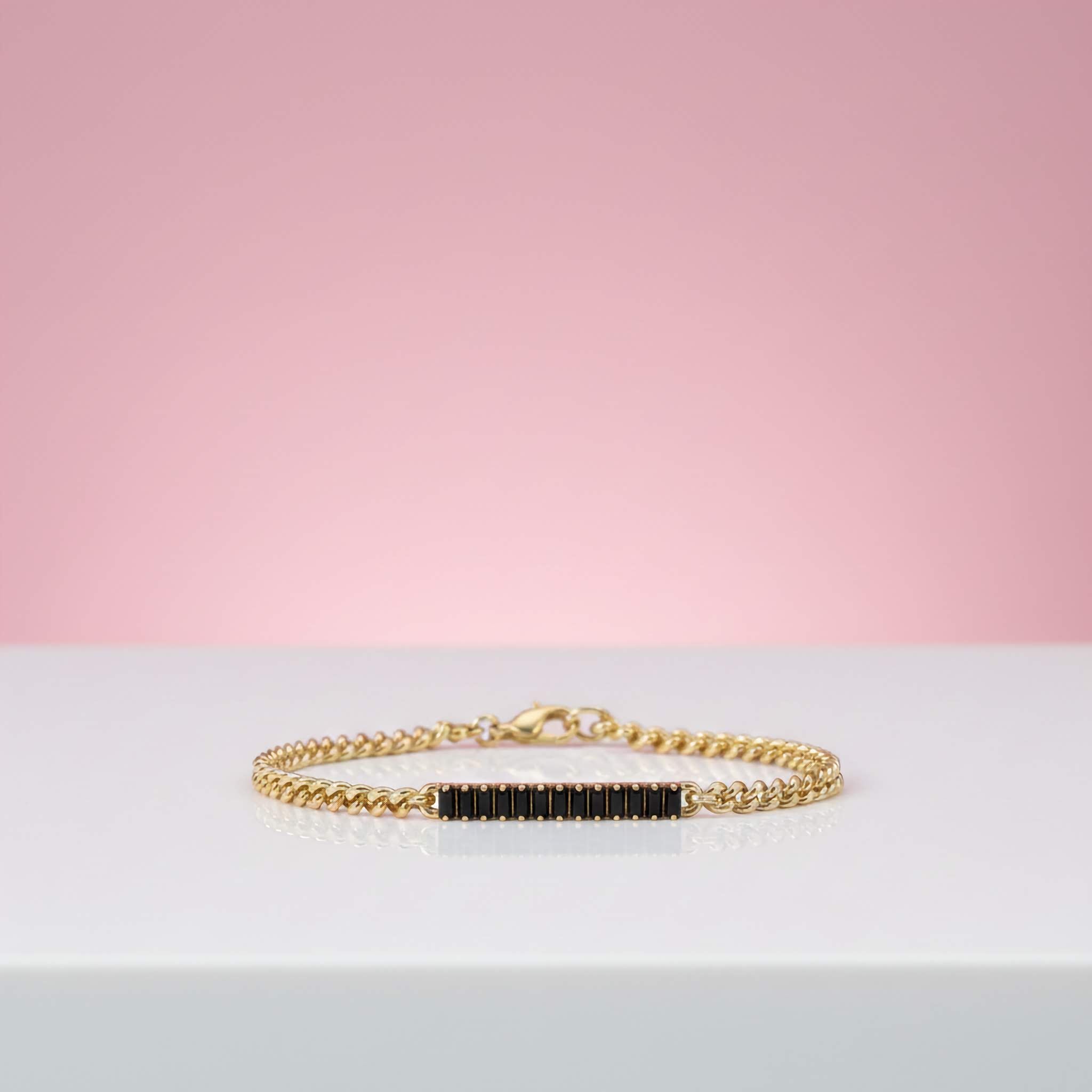 Gold bracelet with black stones on a light gray surface with a pink background