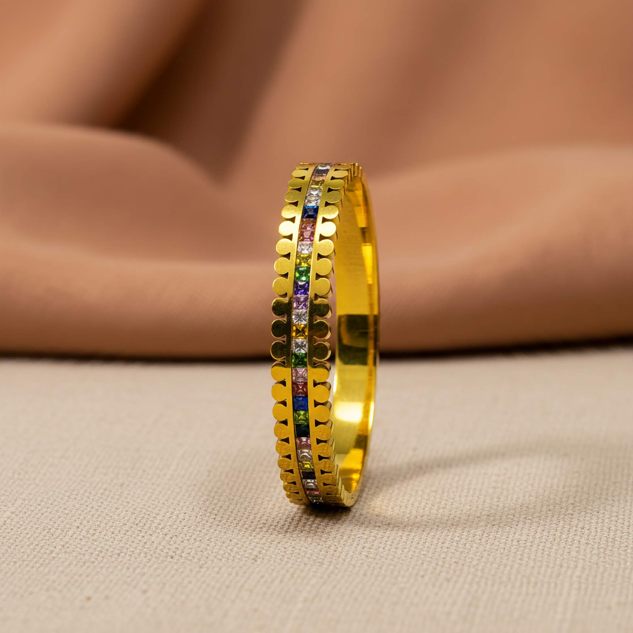 Gold bracelet with colorful stones on a beige surface