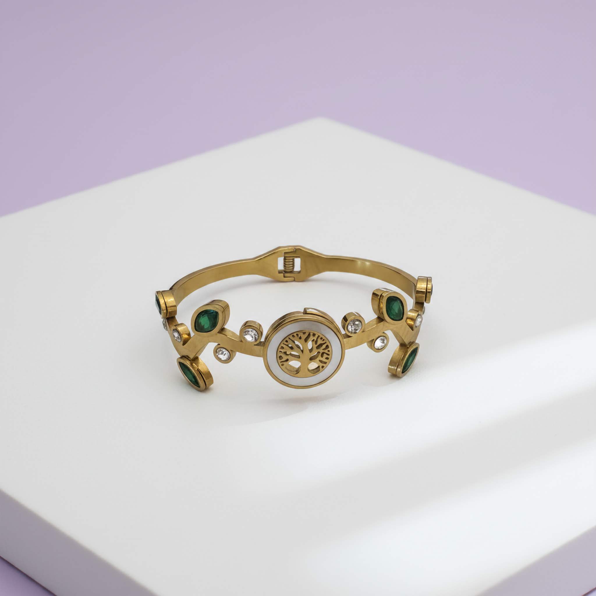Gold bracelet with green gemstones and AD stones with a white centre on a white surface with a purple background