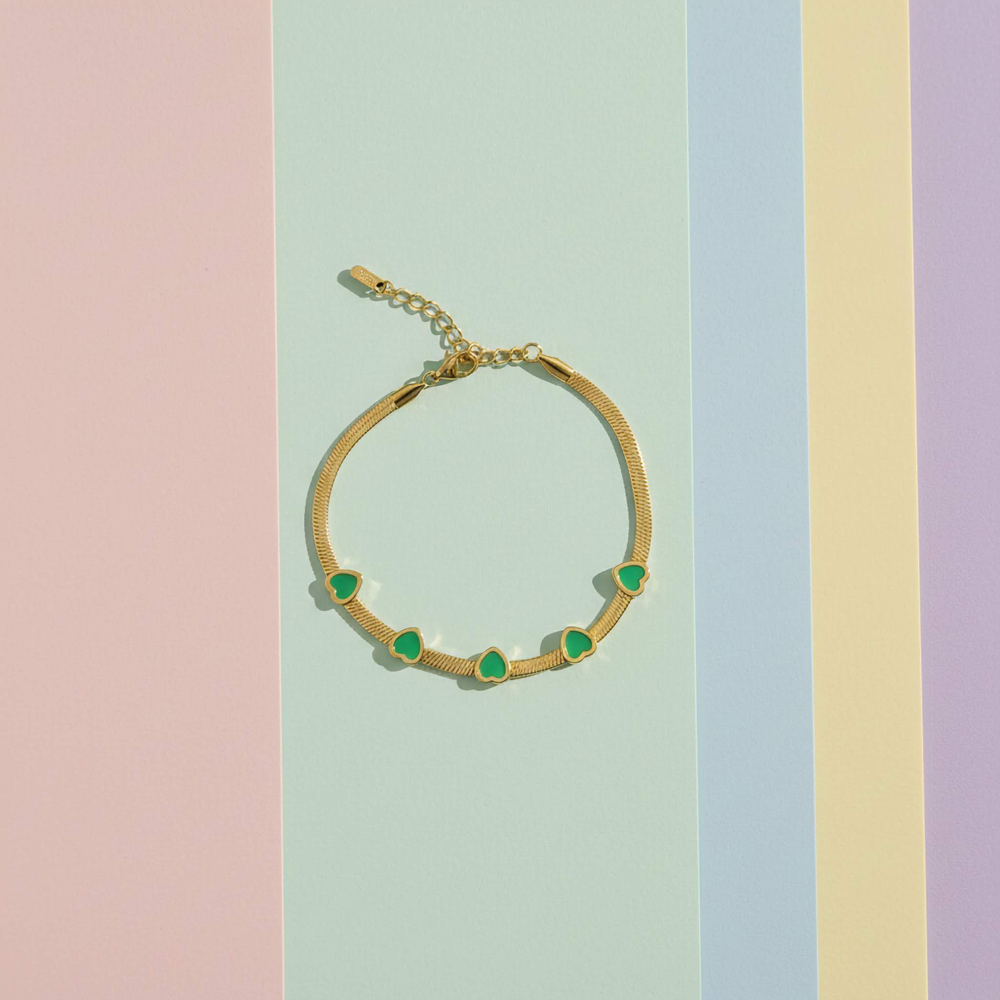 Elegant Green Crystal Bracelet with green heart charms on a pastel striped background