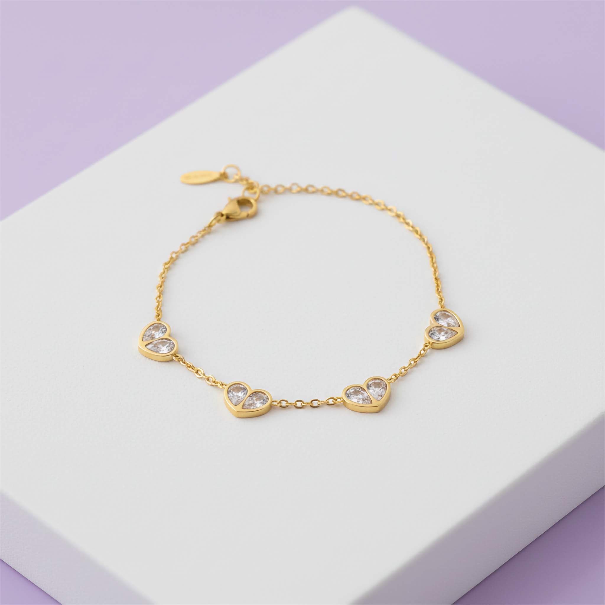 Gold bracelet with heart-shaped crystals on a white box with a purple background
