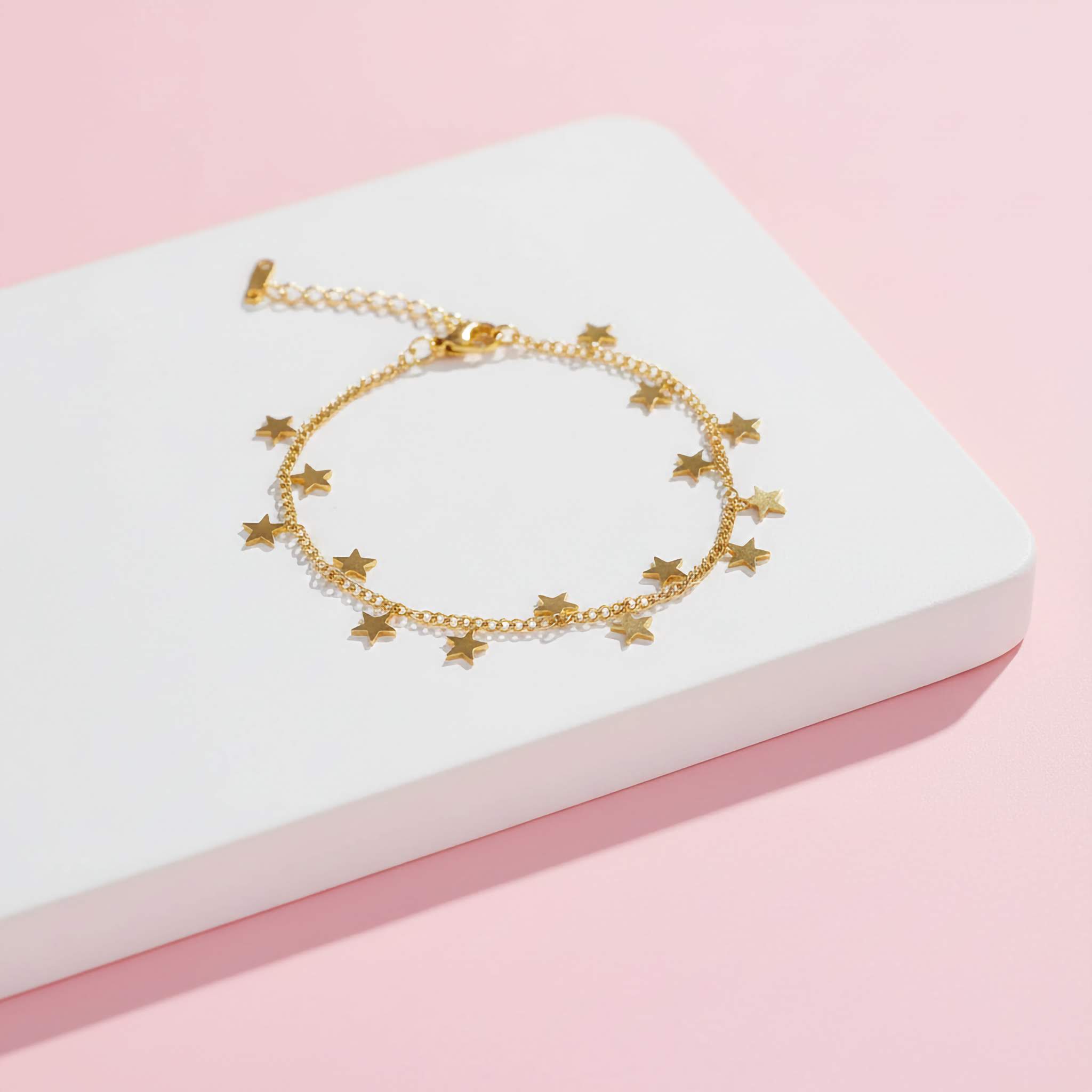 Gold bracelet with star charms on a white box against a pink background