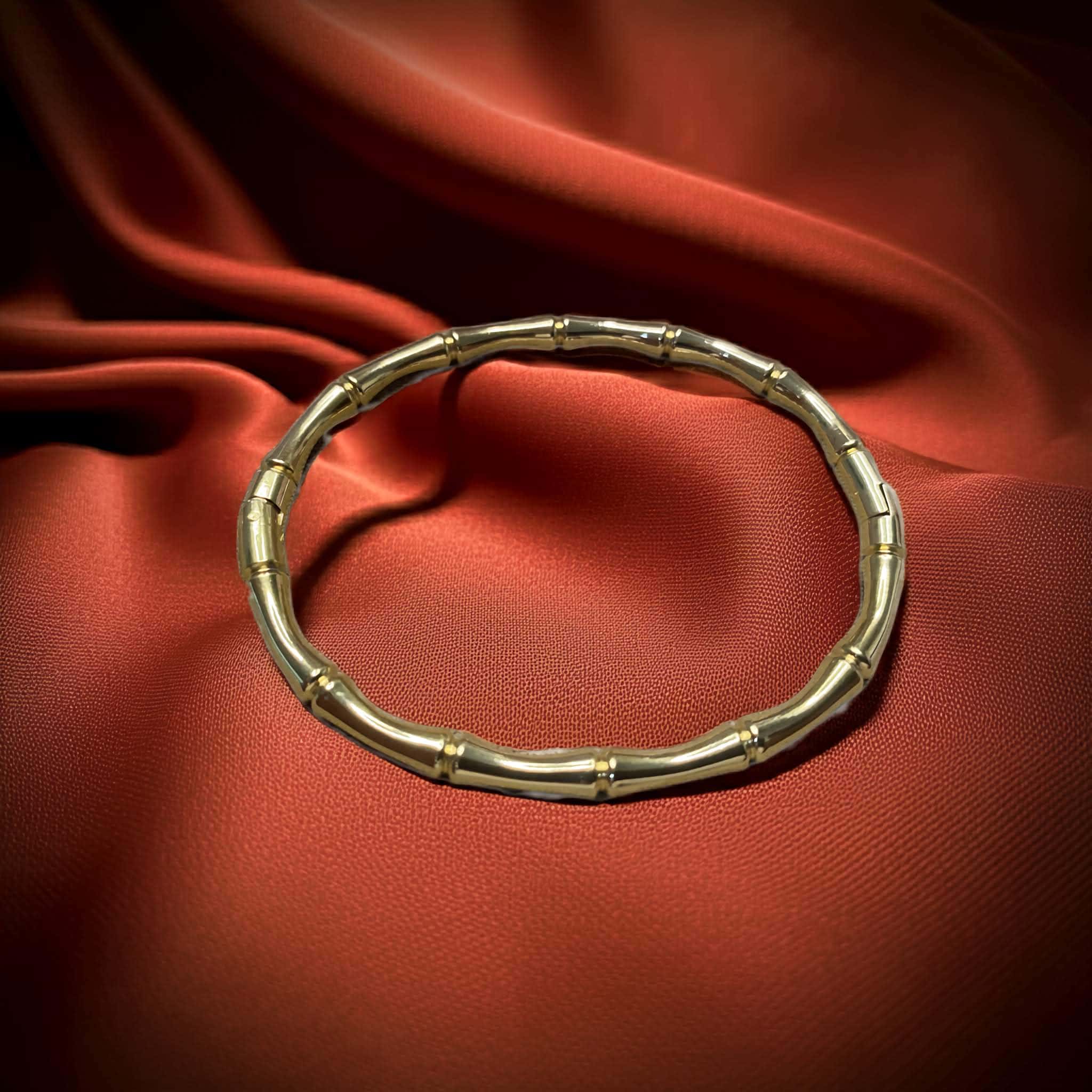Gold plated bamboo-inspired bangle on a red fabric background