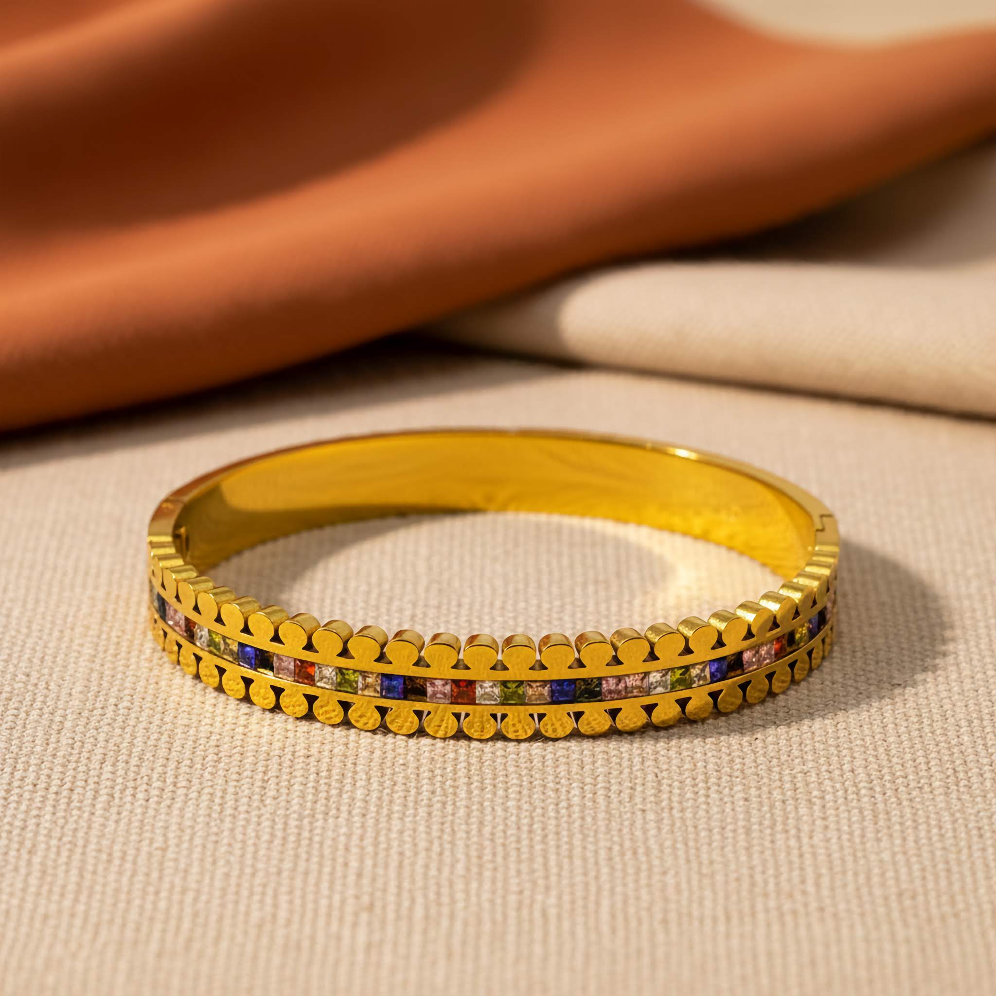 A Gold plated bracelet with colorful stones on a beige fabric background