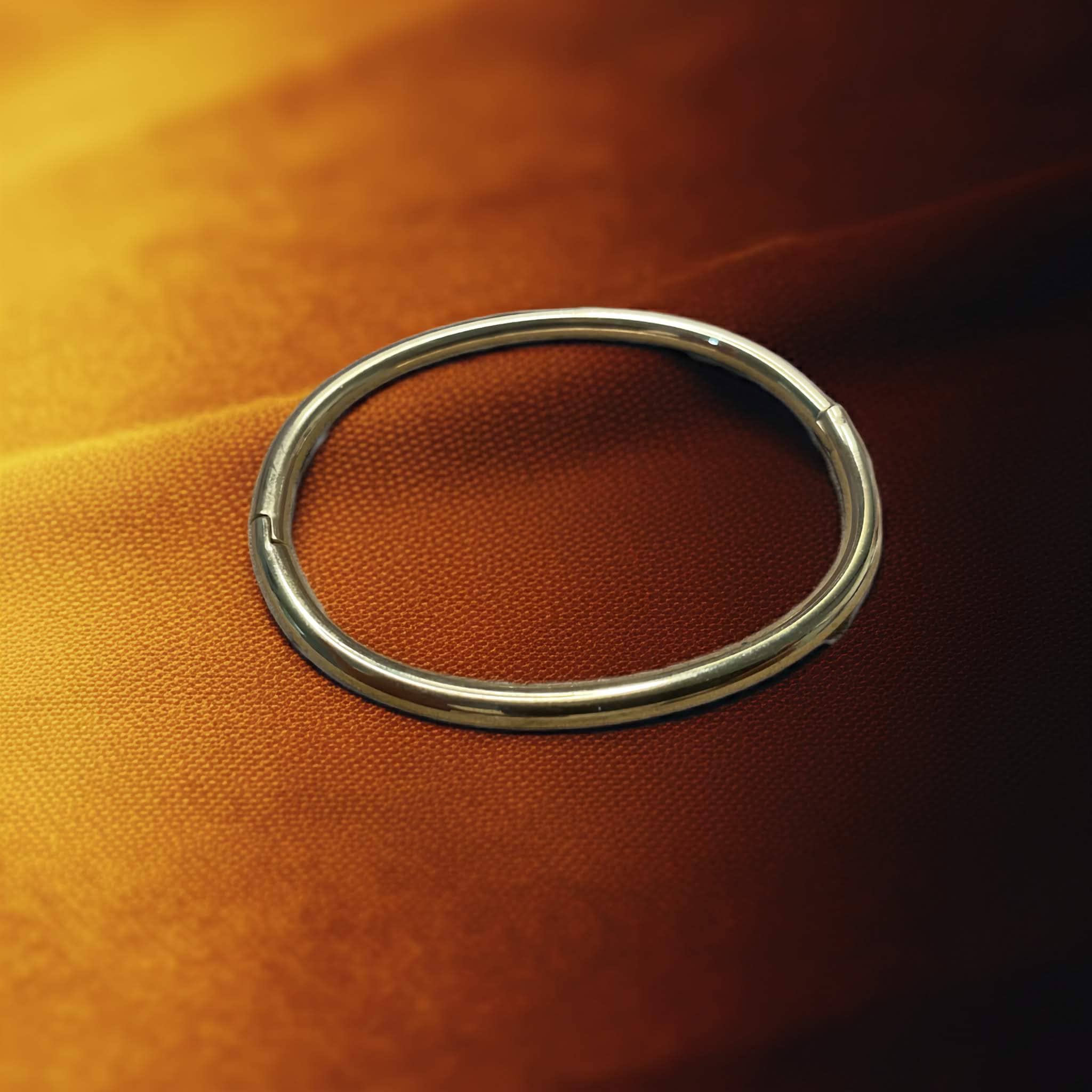 Gold plated simple pipe bangle on a textured orange surface