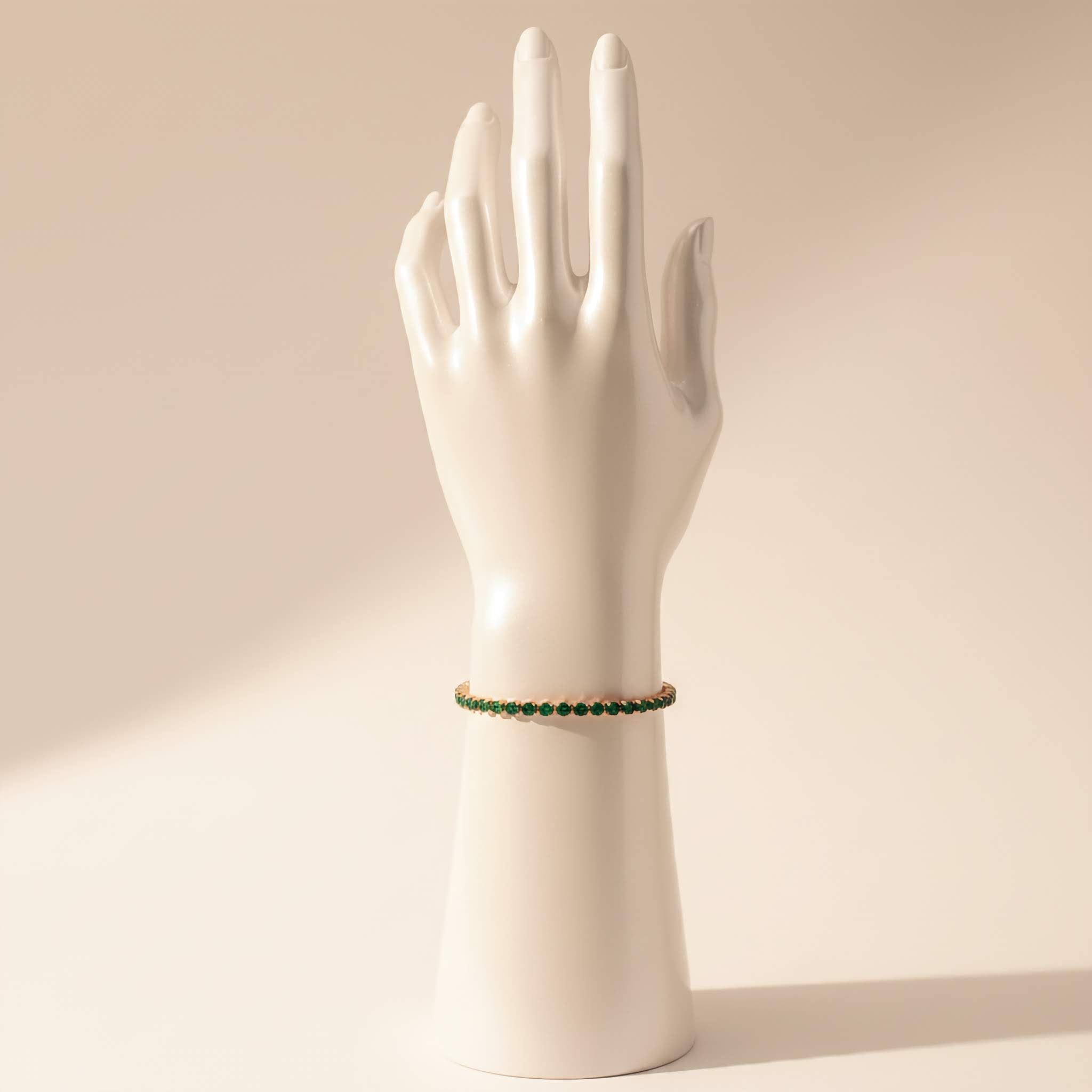 Mannequin hand wearing a green beaded tennis bracelet on a beige background
